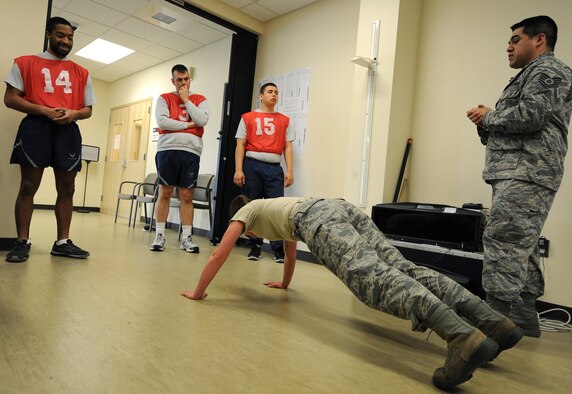 Senior Airman Guinevere Running Wolf and Tech. Sgt. Juan Hernandez demonstrate and brief Airmen on how to do proper push-ups during a physical fitness test at Fairchild Air Force Base, Wash., March 27, 2014. Both Running Wolf and Hernandez are from the 92nd Force Support Squadron. (U.S. Air Force photo by Airman 1st Class Janelle Patiño/Released)