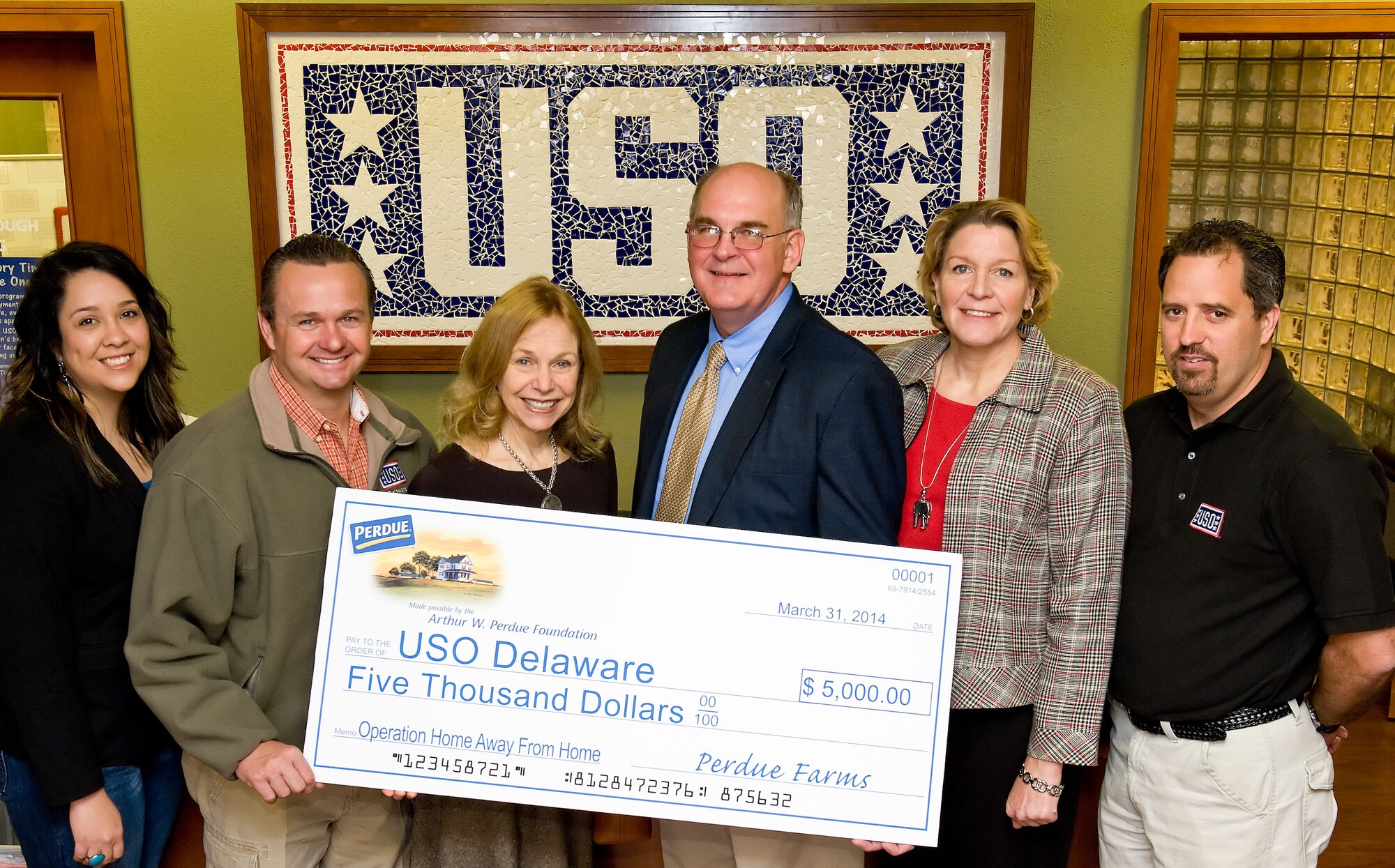 Mitzi Perdue, Arthur W. Perdue Foundation board of directors member, third from the left, presents a $5,000 check to the United Services Organization Delaware March 31, 2014, at the USO lounge on Dover Air Force Base, Del. Accepting the check on behalf of the USO Delaware are, left to right: Yolanda Bottorf, Families of the Fallen support manager for the USO; Bruce Kmiec, USO Delaware operations manager; David McClellan, 512th Maintenance Group honorary commander; Mary Johnson, USO Delaware Advisory Council member; and Bill Flanders, USO Delaware program coordinator. The donation will be used to support programs and services for service men, women and their families. (U.S.  Air Force photo/Roland Balik)