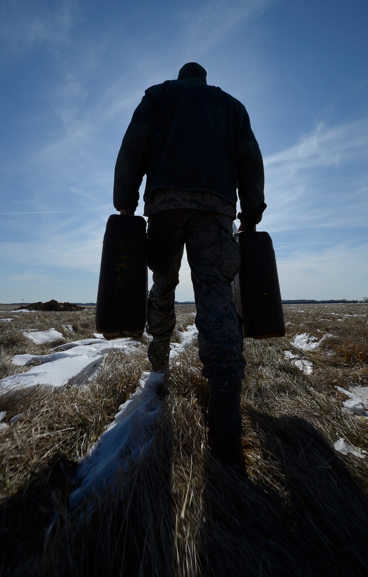 Airman 1st Class Matthew Bizzarro, 436th Civil Engineer Squadron, 'Dirt Boys', carries two cans of diesel fuel through a field with ribbons of snow on the ground on March 21, 2014, at Dover Air Force Base, Del. The fuel is needed to replenish a mini-excavator being used to dig-up a water line. (U.S. Air Force photo/Greg L. Davis)