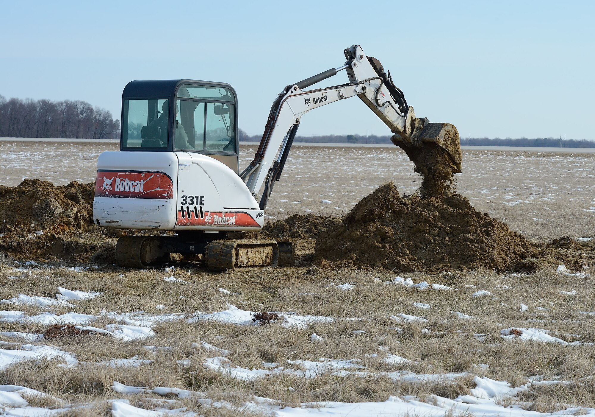 A Bobcat 331E mini-excavator digs up part of a water line near the approach end of runway 32 during a public works project undertaken by the 436th Civil Engineer Squadron, 'Dirt Boys', on March 21, 2014, at Dover Air Force Base, Del. Pockets of snow can be seen in the field during this cold-weather dig. (U.S. Air Force photo/Greg L. Davis)