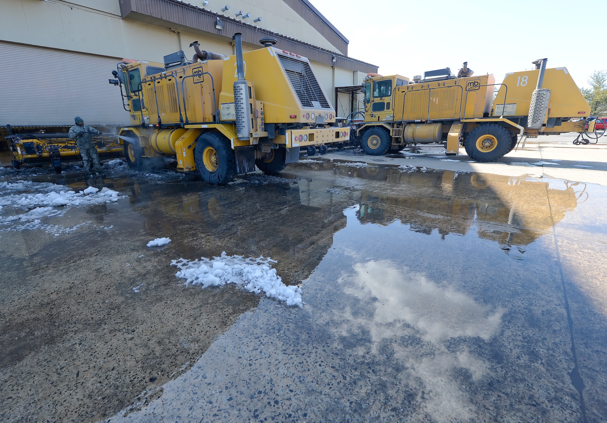 Two bright yellow Oshkosh snow removal machines are cleaned March 20, 2014, in preparation for their return to service after being used extensively at Dover Air Force Base, Del. The equipment belongs to the 436th Civil Engineer Squadron. (U.S. Air Force photo/Greg L. Davis)