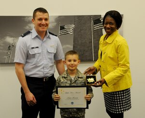 1st Lt. David Smith and Shelly Walker present a Hero Award to Käal Mocanu at the Military & Family Support Center on Joint Base Andrews, Md., April 24. Käal, son of retired Master Sgt. Brandon Mocanu and Tech. Sgt. Amanda Mocanu, M&FSC readiness NCO in charge, received the award for his brave actions when his father collapsed in their home in February. Smith is the 11th Force Support Squadron section commander and Walker is an M&FSC community readiness consultant. (U.S. Air Force photo/Airman 1st Class Ryan J. Sonnier)