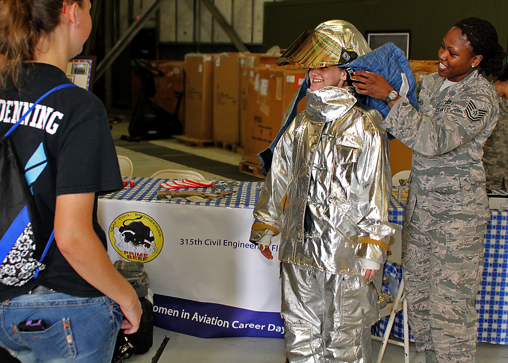 Tech Sgt. Mendy Dillard, 315th Civil Engineer Flight firefighter, helps a Junior Reserve Officers' Training Corps cadet try on firefighter protective gear at the Joint Base Charleston Women in Aviation Career Day April 29. About 90 8th and 9th-grade girls from Charleston area schools visited base to learn about jobs in aviation and meet successful women in aviation career field. (U.S. Air Force photo by Michael Dukes)