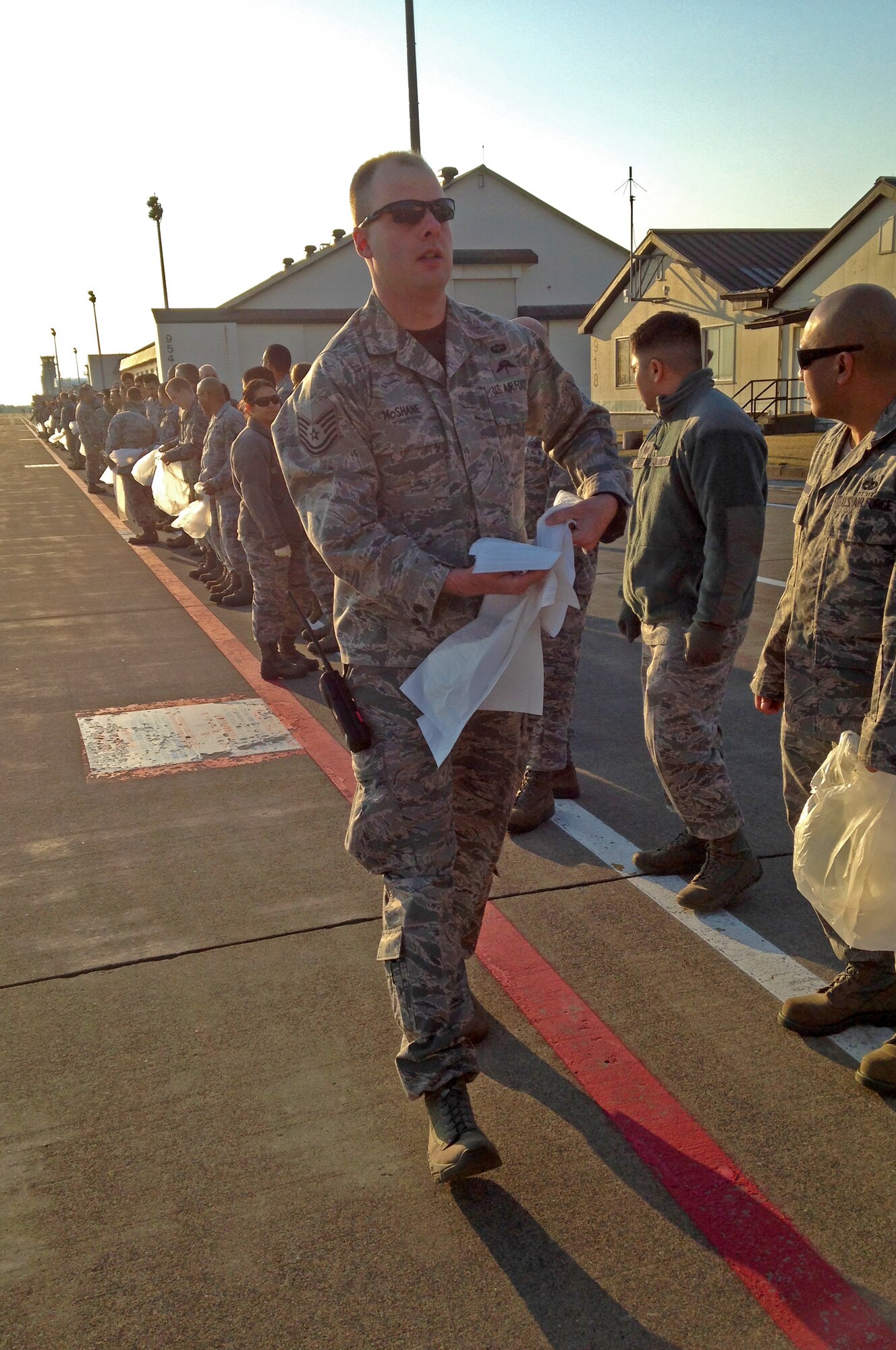 U.S. Air Force Tech. Sgt. Stephen McShane, 35th Aerospace Medicine Squadron NCO in charge of aerospace and operational physiology team, hands out bags to Airmen stationed at Misawa Air Base, Japan in preparation of the first annual foreign object damage walk on April 25, 2014.  Removal of FOD from the flightline helps eliminate unfortunate mishaps occurring to the aircraft while taxiing the runways. (U.S. Air Force photo by Tech. Sgt. April Quintanilla)