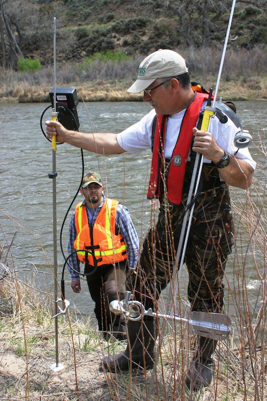 EMBUDO, N.M., -- USGS Hydrologist George Seiber holds up two different instruments for measuring stream flow.  The left one uses acoustics to measure; the instrument on the right is a traditional mechanical current meter.  

