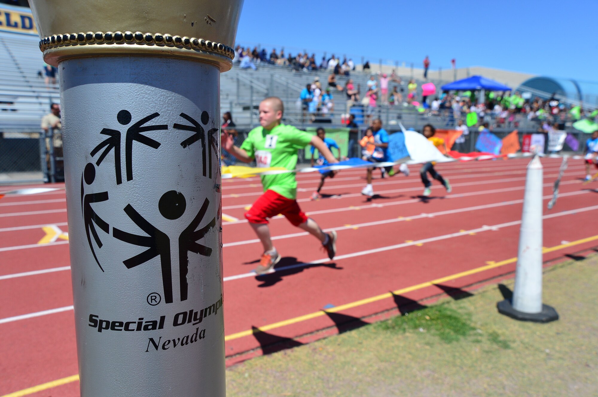 Children competing in the 50-meter race past the Nevada Special Olympics torch at Cheyenne High School in Las Vegas May 1, 2014. More than 240 Airmen from Nellis and Creech Air Force Bases volunteered their time during the two-day event to help unify the community and set an example through fitness and sports play.
