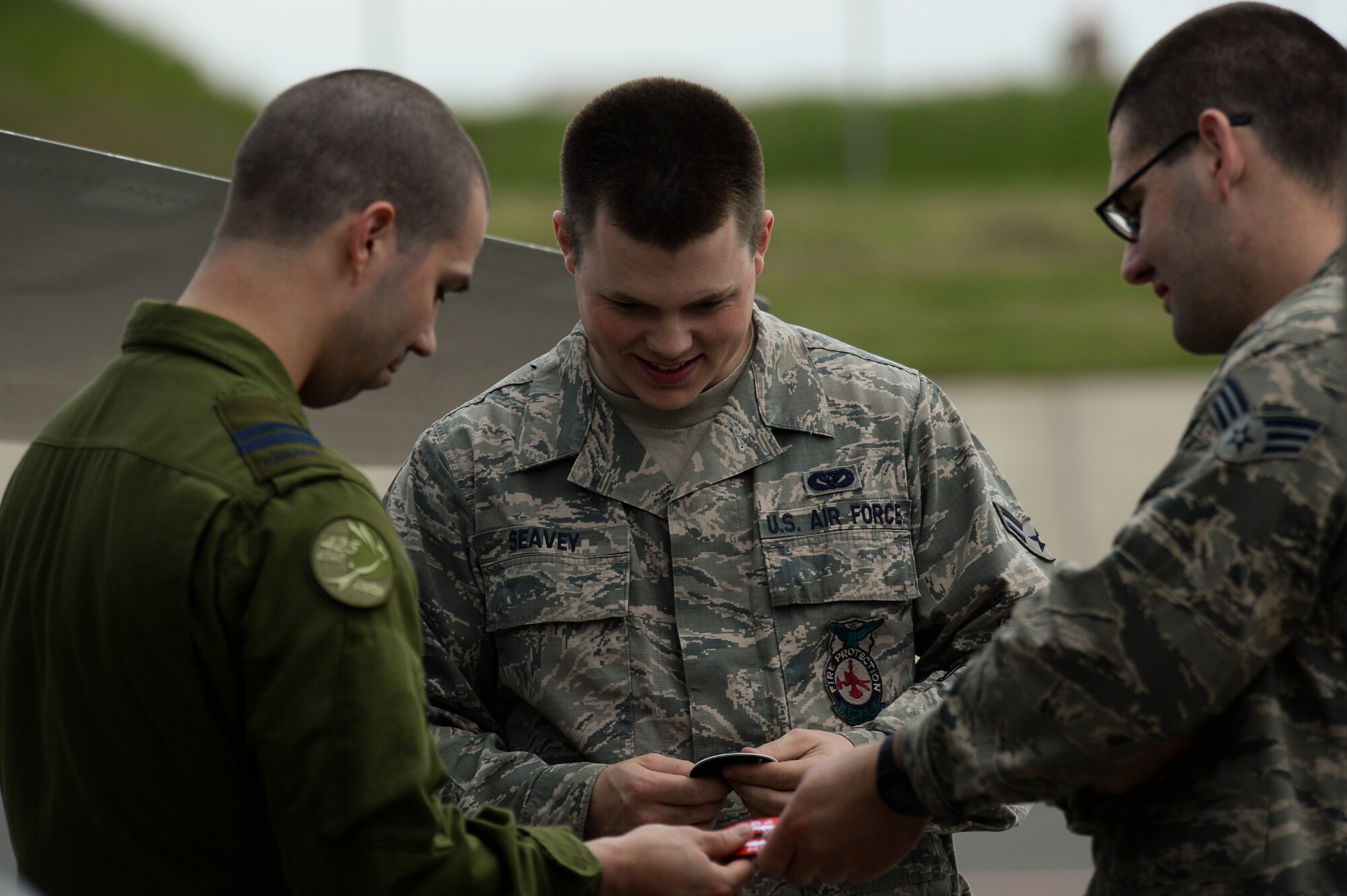 U.S. Air Force Airman 1st Class Jason Seavey (center), a 52nd Civil Engineer Squadron fire protection apprentice from Baileyville, Maine, and Senior Airman Steven Mueller, a 52nd CES fire protection journeyman from Kerrville, Texas, exchange patches with a pilot from the Royal Canadian Air Force May 1, 2014, at Spangdahlem Air Base, Germany.  The 52nd Fighter Wing hosted members of the RCAF as they traveled to Romania to support combined NATO exercises as part of a persistent presence in the region. (U.S. Air Force photo by Senior Airman Rusty Frank/Released)