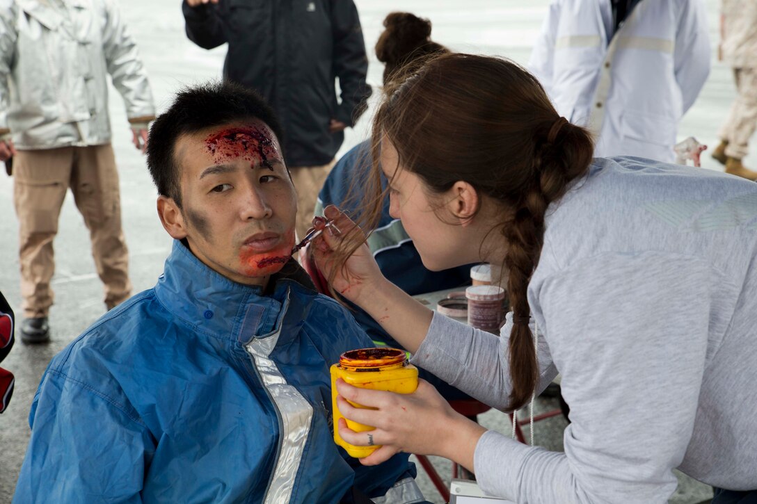 Seiya Chinen, left, has artificial blood and makeup applied, a technique known as moulage, April 24 at the Naha Military Port. During the exercise, local and military police, fire fighters and emergency response personnel executed a series of planned training events in response to the simulated crash of a military aircraft in an urban area. The makeup and gore was used to make Off-Base Aircraft Mishap Exercise 2014 as realistic as possible. Chinen is a firefighter with the Naha City Fire Department.