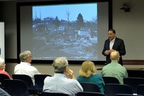 Howard Donaldson, North American Aerospace Defense Command and U.S. Northern Command judge advocate office, briefs about his experiences with the American Red Cross after he and his family lost their house, shown pictured on the screen, in the Waldo Canyon Fire of 2012.