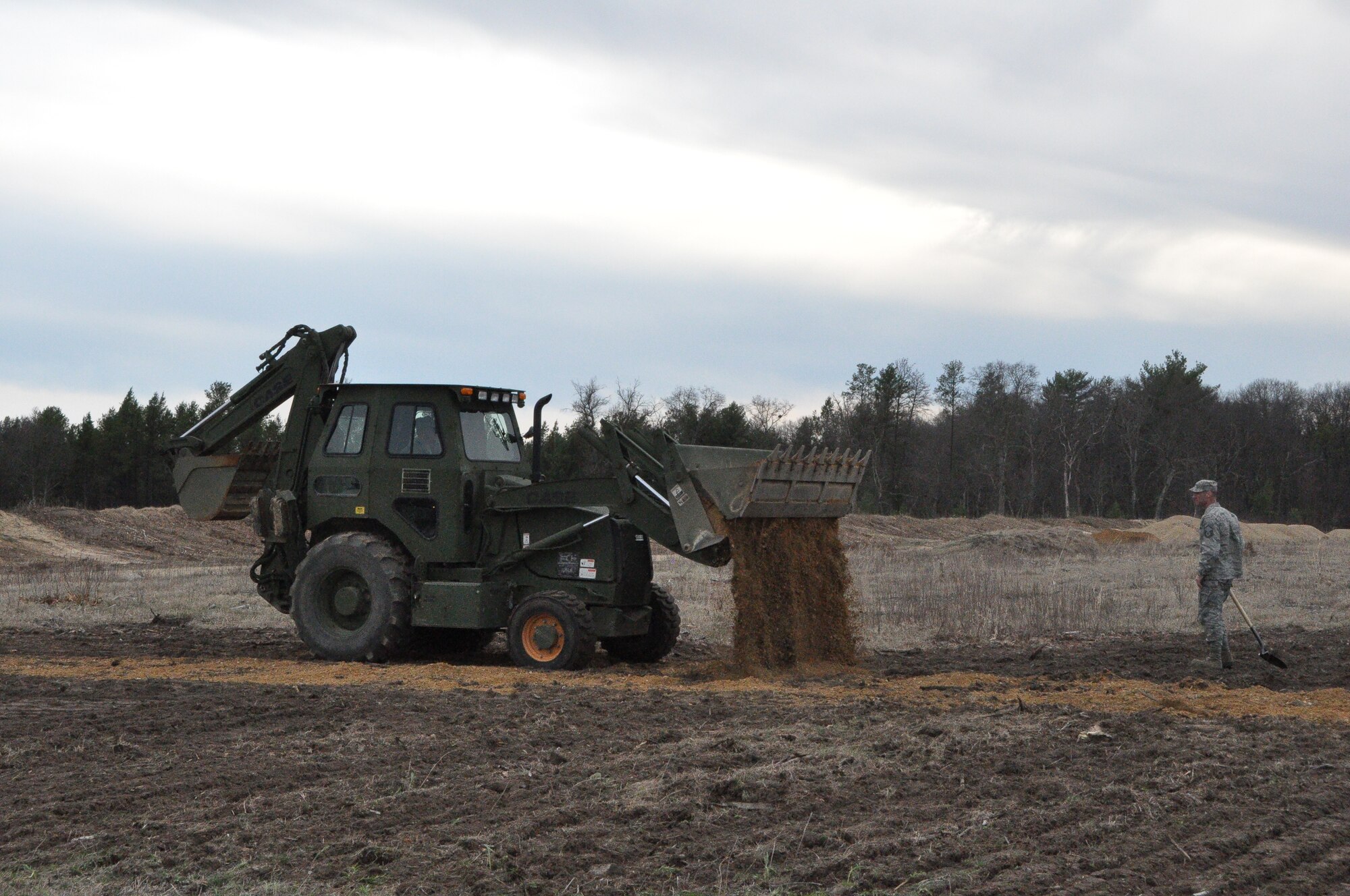 Airman from the 433rd Civil Engineer Squadron level the ground at Fort McCoy Wis. April 26 preparing for the bed down of a Forward Operating Base in support of Exercise Patriot Warrior 2014. MSgt Curtis Wilson, CE Structures Specialist, drives the backhoe with a clam shell on the front while MSgt Michael Shedrock, CE Electrical Specialist, spots the equipment. Safety, wingman concept, and teamwork are always paramount, especially in these conditions and climate. (U.S. Air Force photo by 1st Lt. Denise Haeussler)