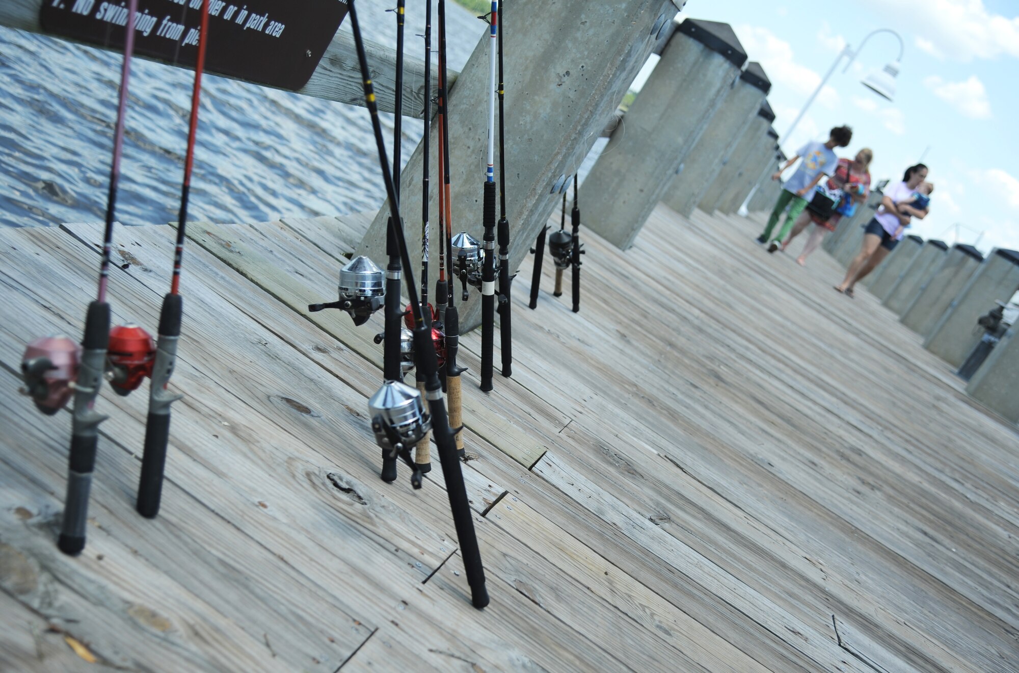 Fishing poles lean against the pier railing as families approach for the Kids Spring Fishing Rodeo May 3, 2014, at the marina, Keesler Air Force Base, Miss.  The event was hosted by the outdoor recreation center. (U.S. Air Force photo by Kemberly Groue)