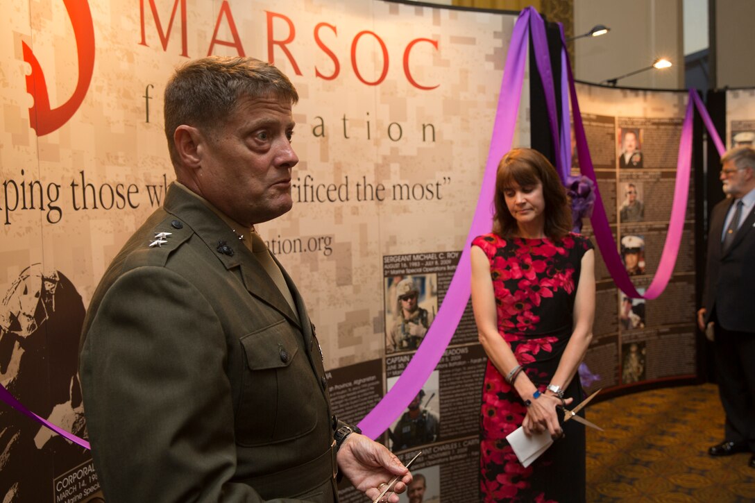 Major Gen. Mark A. Clark, commanding general of U.S. Marine Corps Forces Special Operations Command, and Sarah Christian, director of operations for the MARSOC Foundation prepare to cut a purple ribbon to unveil the MARSOC Foundation’s mobile memorial wall, during ‘Honor the Fallen,’ a one-of-a-kind event, April 25, to honor all Marines, sailors and civilian Marines lost at home and abroad since MARSOC’s inception. The significance of the mobile memorial wall is to honor the Marines, sailors and civilian Marines who lost their lives while serving with MARSOC, as well as to honor their families, sharing their stories with as wide of an audience as possible. “The hope is that people will see the wall, reflect upon the service and sacrifice of these men & women and their families, and hopefully try to learn more about each of them,” said Christian.  “The MARSOC Foundation also hopes that it will remind the American public that even though military missions are not being talked about on the news, there are still brave men and women stationed throughout the world protecting our country and our freedom.”
