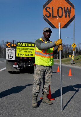 Airman 1st Class Michael Ramseur, 773d Civil Engineer Squadron structures apprentice, signals traffic while 773d CES personnel repaint lines on Provider Drive at Joint Base Elmendorf-Richardson, Alaska, April 30, 2014. The lines on JBER are repainted every year due to the wear and tear from snow plows during the winter. (U.S. Air Force photo/Airman 1st Class Tammie Ramsouer)