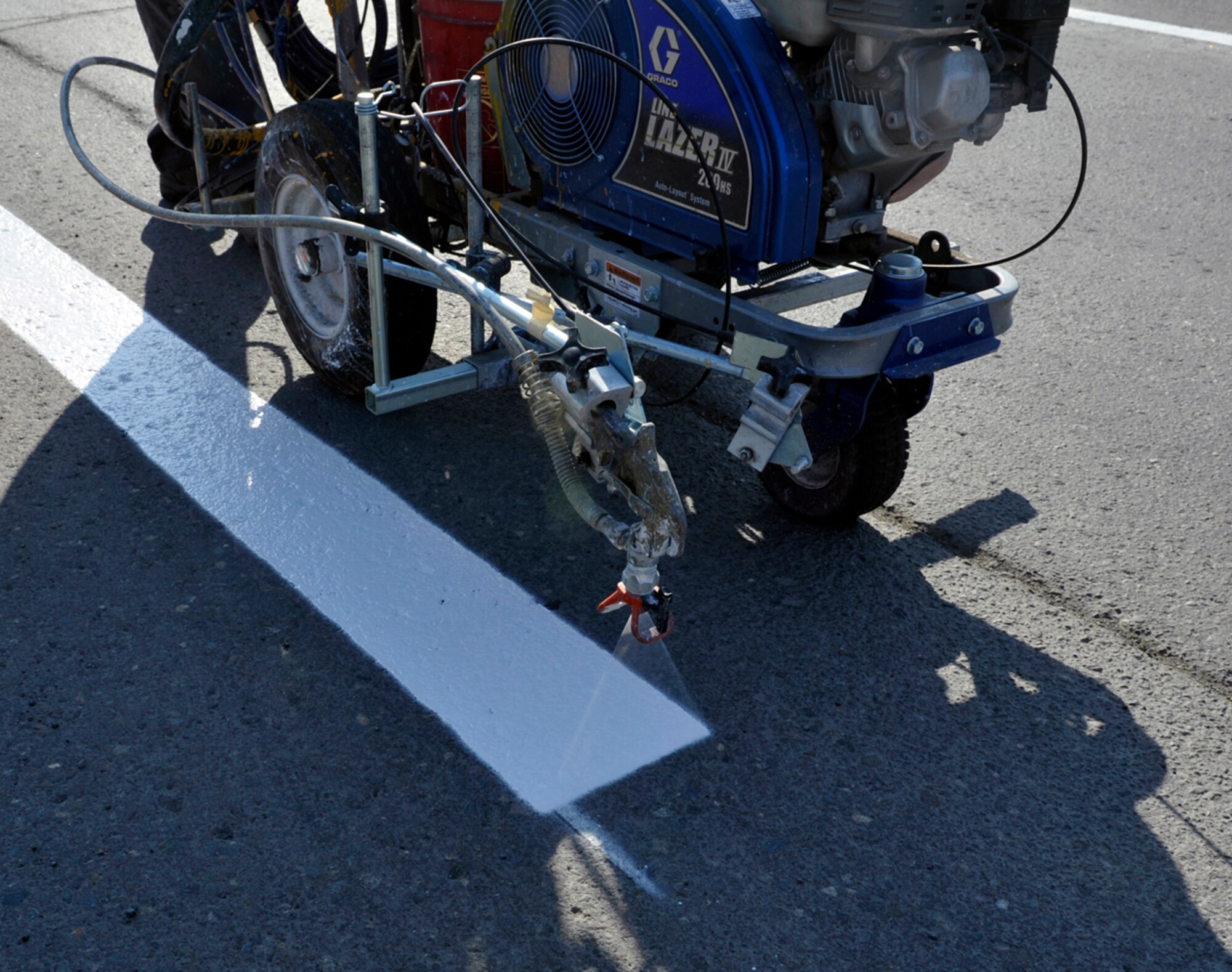 Matthew Carl Michaelis, 773d Civil Engineer Squadron sign painter, sprays lines with a striping machine on Joint Base Elmendorf-Richardson, Alaska, April 30, 2014. The roads on JBER are cleaned before the lines are painted, so the paint can adhere to the asphalt. Glass beads are added to the paint as a reflector for drivers to see the lines at night. (U.S. Air Force photo/Airman 1st Class Tammie Ramsouer)
