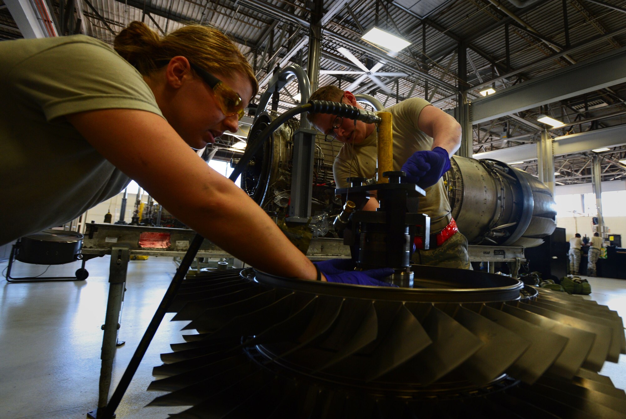 [From Left] U.S. Air Force Airman 1st Class Sarah Benedict and Senior Airman James Hafner, 20th Component Maintenance Squadron aerospace propulsion technicians, prepare the fan of a F110-General Electric-129 jet engine for measurements during Operational Readiness Exercise Weasel Victory 14-06 at Shaw Air Force Base, S.C., May 6, 2014. The two established proper installation of the rotating fan shaft to ensure the engine can meet its maximum fan speed at 8,200 rotations per minute. (U.S. Air Force photo by Airman 1st Class Jensen Stidham/Released)