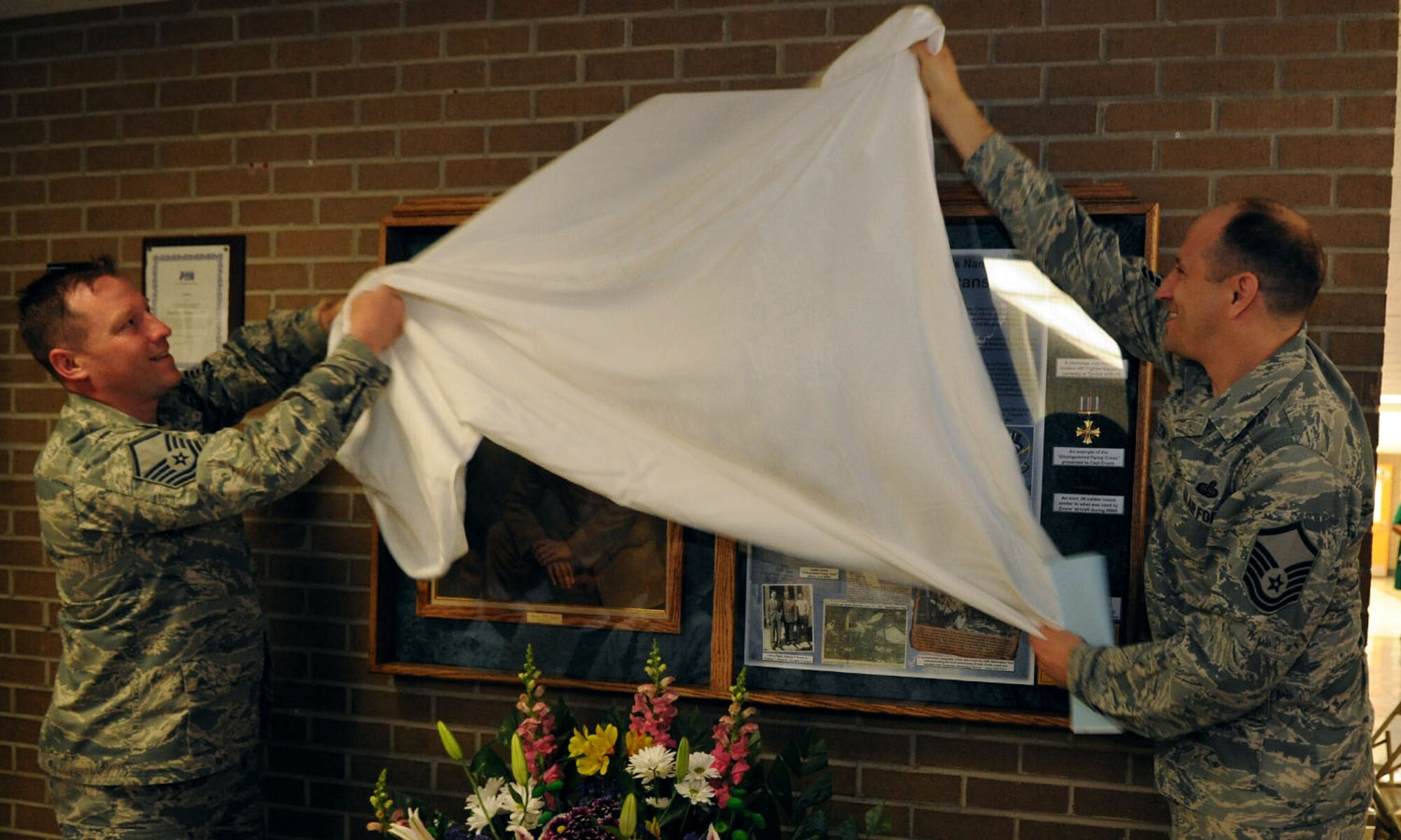 Master Sgts. Phillip Allen and Matt Cagle, 744th Communication Squadron plans and program managers, unveil a memorial display case specially made for the Francis T. Evans Elementary School May 2, 2014. The case displays memorabilia of the school’s namesake, Capt. Francis T. Evans, Jr. and is located at the school just outside of Joint Base Andrews, Md. (U.S. Air Force photo/Aimee Fujikawa)
