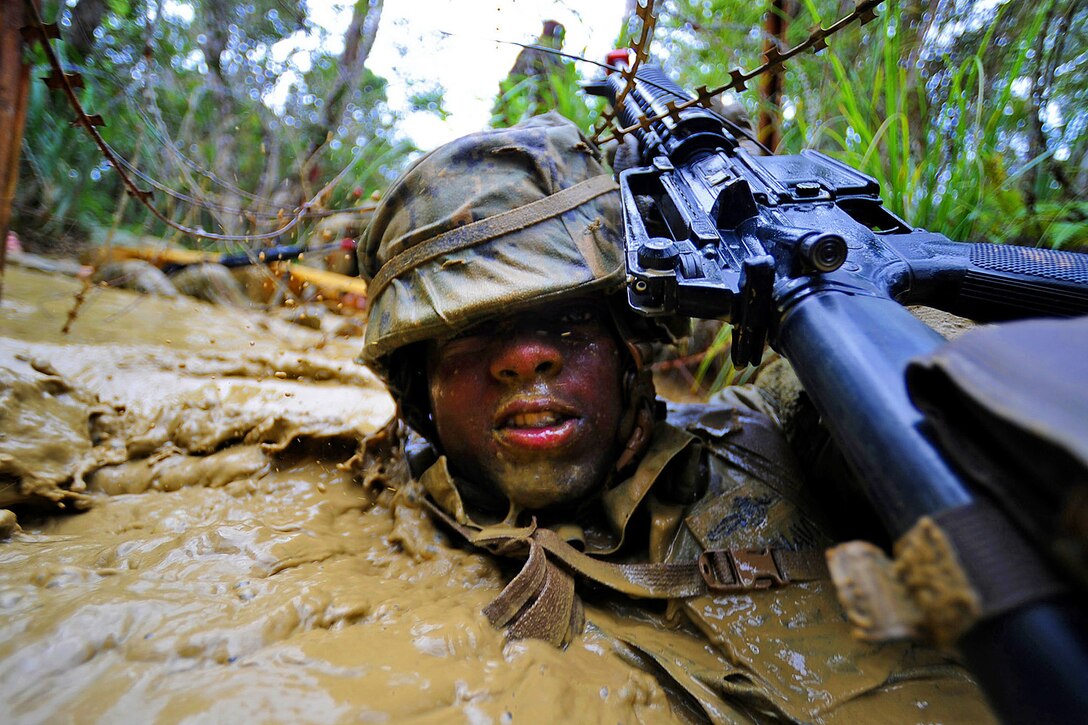 U.S. Navy Petty Officer 2nd Class Dwayne Watson uses his weapon to push concertina wire away from his face while running a six-hour endurance course at the Marine Corps Jungle Warfare Training Center in Okinawa, Japan, Sept. 22, 2013. Watson is assigned to Naval Mobile Construction Battalion 3.  
