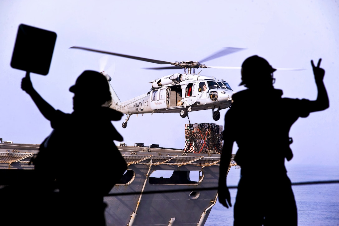 U.S. Navy Seaman Kendahl Chmara, left, signals to the USNS Arctic as U.S. Navy Petty Officer 3rd Class Matthew Michela gives commands to riggers during a replenishment aboard the aircraft carrier USS Harry S. Truman in the U.S. 5th Fleet area of responsibility, Sept 13, 2013.  
