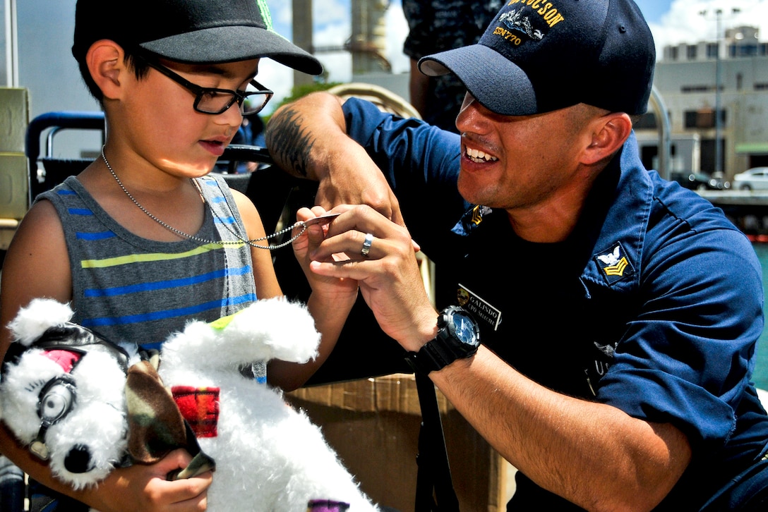 U.S. Navy Chief Miguel Galindo shows his identification tags to his son at a luncheon on Joint Base Pearl Harbor-Hickam in Pearl Harbor, Hawaii, Sept. 5, 2013, before he leaves for a deployment to the western Pacific region. Galindo is assigned to the attack submarine USS Tucson.  
