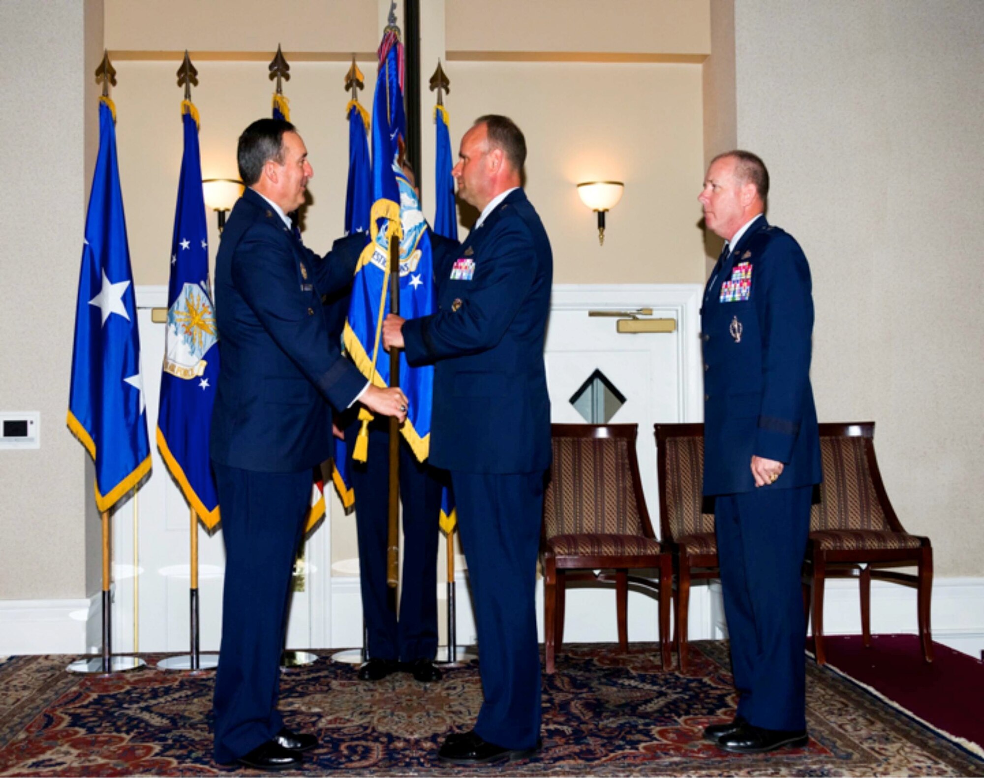 Lt. Gen. Stephen P. Mueller, Inspector General of the Air Force, presents the Air Force Office of Special Investigations command flag to Brig. Gen. Keith M. Givens, the newest AFOSI commander, during a change-of-command ceremony while Brig. Gen. Kevin J. Jacobsen, former AFOSI commander, looks on. 