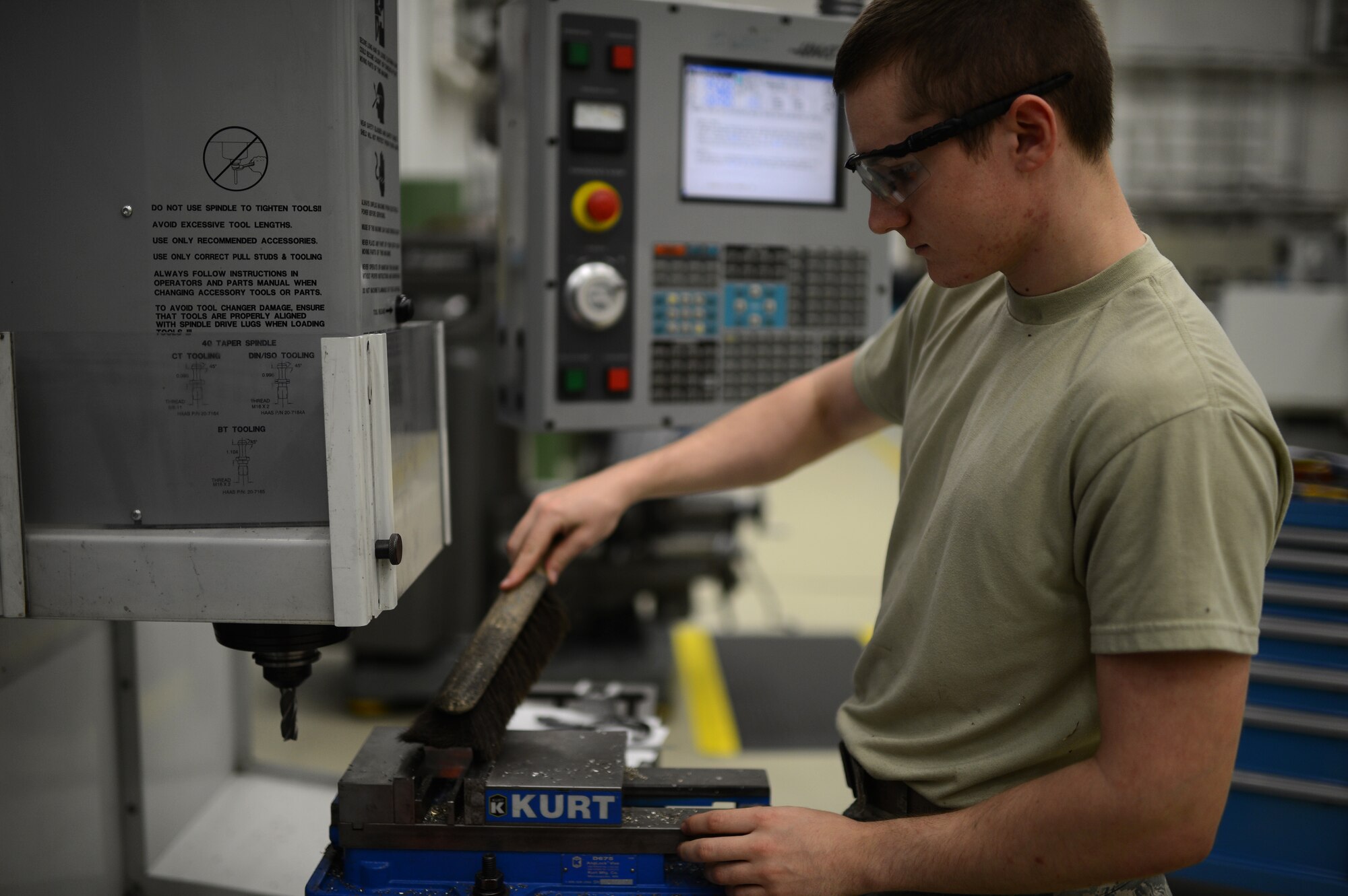 U.S. Air Force Airman Alex Larkin, 52nd Equipment Maintenance Squadron aircraft metals technician from Queen Creek, Ariz., brushes away metal shavings inside the fabrication flight shop at Spangdahlem Air Base, Germany, May 6, 2014. The workstation must be clean of debris for technicians to make accurate measurements when carving and cutting blocks of steel to be used to fix broken mechanical parts. (U.S. Air Force photo by Senior Airman Gustavo Castillo/Released)  