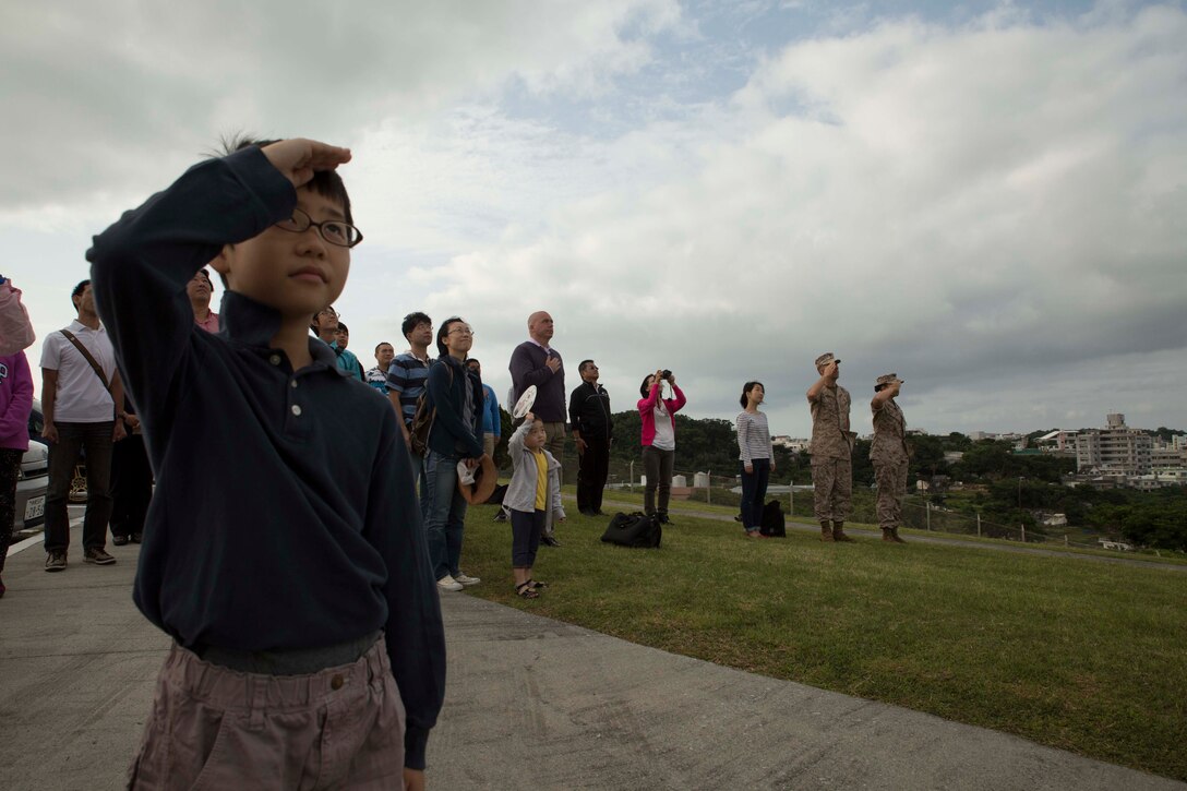 An Okinawa child salutes the national ensigns of the U.S. and Japan April 29 at Camp Foster during a community outreach seminar called Marine Corps 101. The event allows Okinawa citizens the opportunity to learn the history of the U.S. Marine Corps and see military life on the installations. The tour is a regular function that helps strengthen ties between the two nations. 