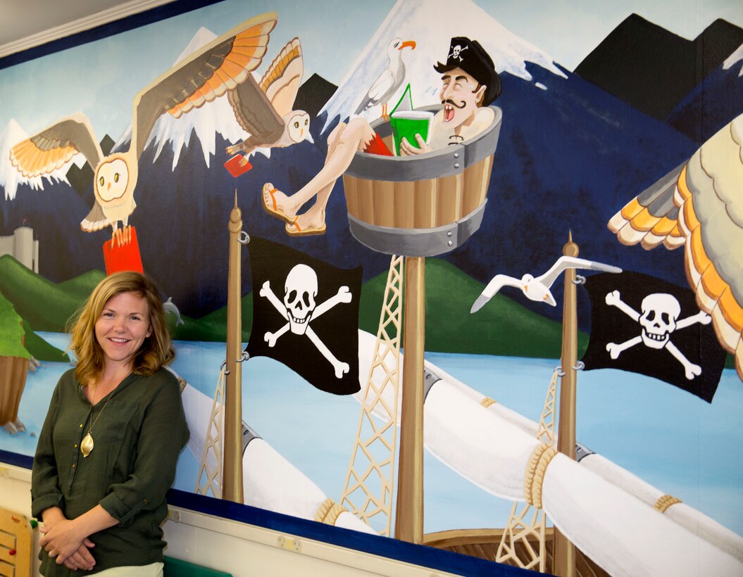 Gwyn Korpi, a military spouse and graphic designer, stands near a mural she painted at the at the children’s area of the Harriotte B. Smith Library aboard Marine Corps Base Camp Lejeune. The mural is designed to pique children’s interests with a fairy tale world that could be the setting of many works of children’s fiction. 