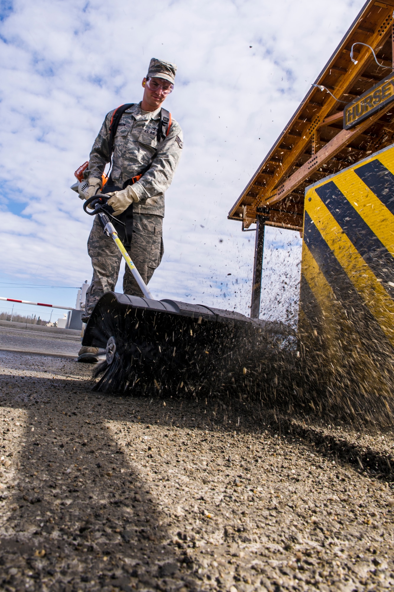 Senior Airman Brandon Johnson, 354th Civil Engineer Squadron pavements and construction journeyman, sweeps away gravel in front of Hursey Gate April 22, 2014, Eielson Air Force Base, Alaska. The Dirt Boyz clean up gravel so Icemen can drive around base safely. (U.S. Air Force photo by Senior Airman Joshua Turner/Released)