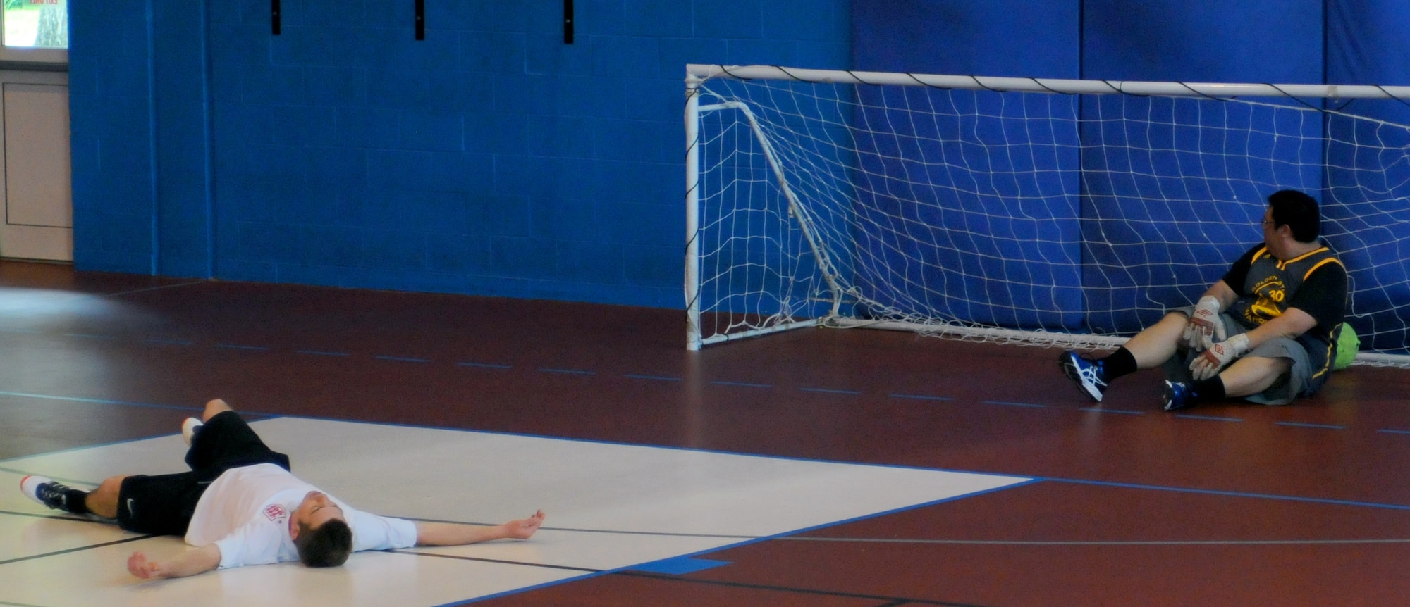 Geoff Gough, left, 100th Civil Engineer Squadron electrician from Thetford, England, lies exhausted on the floor after scoring the final goal of the match against goalie Joseph Cunningham,100th Force Support Squadron civilian payroll technician from Phoenix, Arizona, May 6, 2014, during an indoor soccer championship on RAF Mildenhall, England. The 100th CES team won 8-6 after playing the entire match with no substitution players available. (U.S. Air Force photo by Tech. Sgt. Neal X. Joiner/Released)