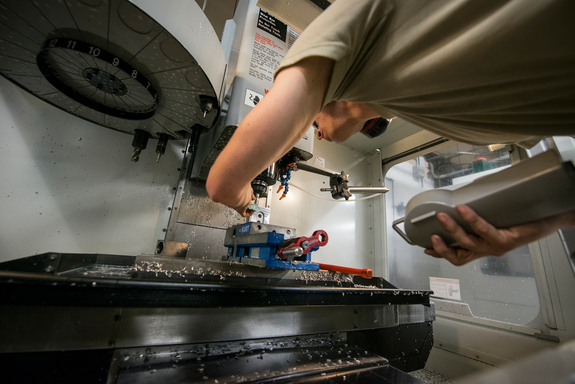 U.S. Air Force Senior Airmen Mark Jensen, 23d Equipment Maintenance Squadron aircraft metals technology journeyman, adjusts a CNC mill at Moody Air Force Base, Ga., April 30, 2014. The CNC mill is an automated machining tool that allows Airmen to program commands for precision cuts. (U.S. Air Force photo by Airman 1st Class Ryan Callaghan/Released)