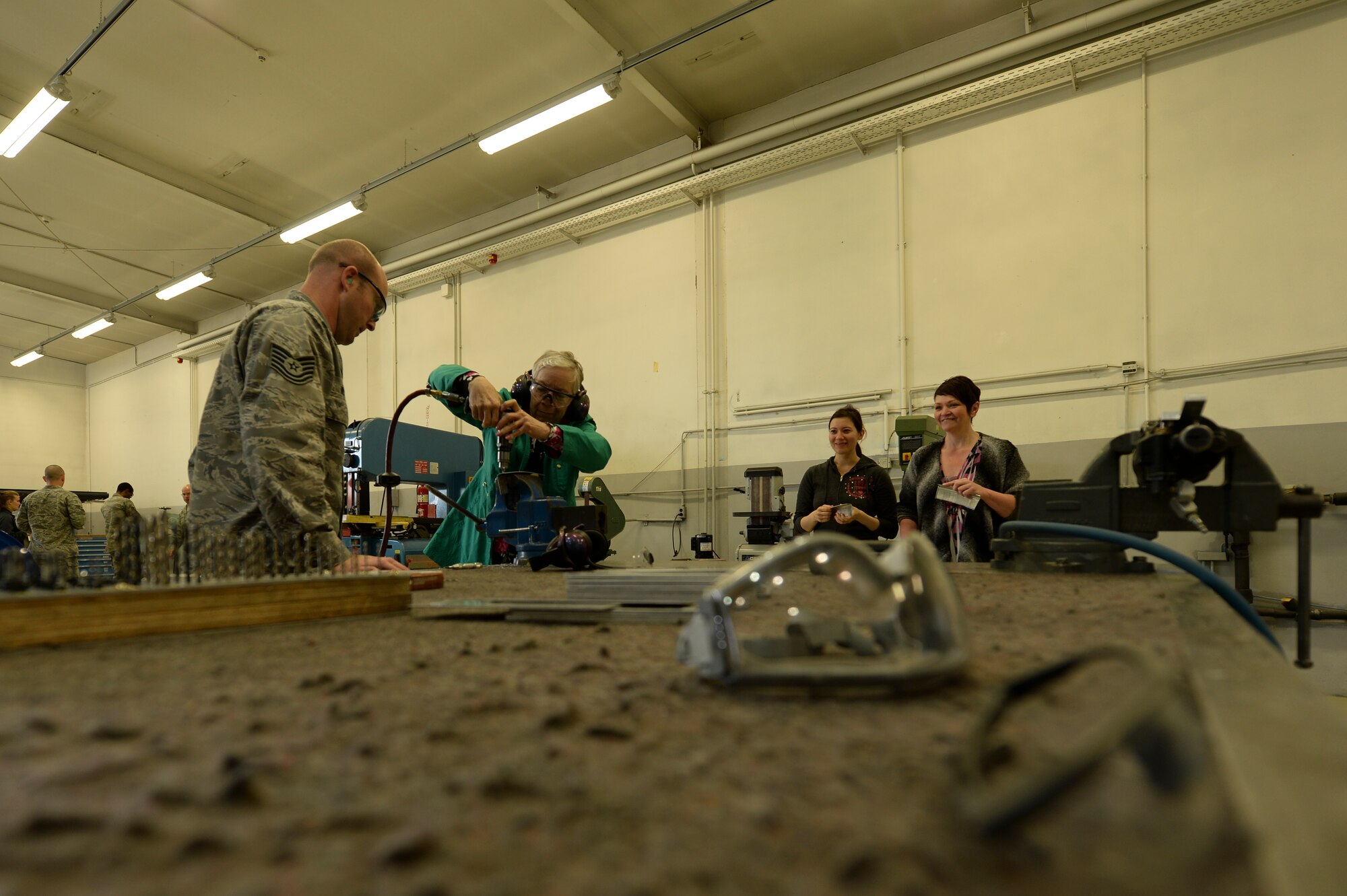 U.S. Air Force Tech. Sgt. Robby Worley, a 52nd Equipment Maintenance Squadron aircraft structural maintenance craftsman form Littlerock, Calif., instructs a spouse how to drill a hole in a piece of sheet metal during the 52nd Maintenance Group spouses tour May 7, 2014, at Spangdahlem Air Base, Germany. As a part of the tour, the spouses saw how the fabrication flight directly affects the base’s flying mission. (U.S. Air Force photo by Senior Airman Rusty Frank/Released)
