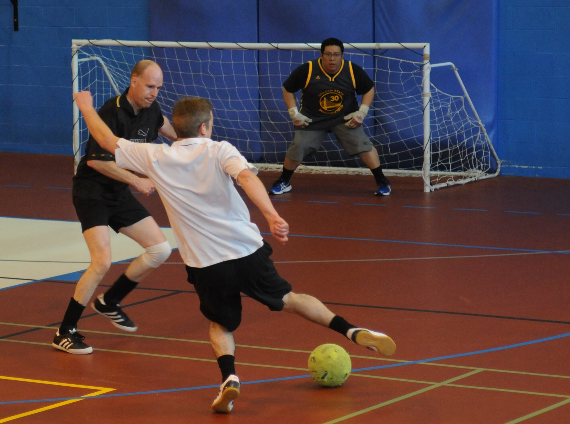 Geoff Gough, center, 100th Civil Engineer Squadron electrician from Thetford, England, moves the ball into scoring position as Gary Butcher, left, 100th Force Support Squadron accounting technician from Cambridge, England, defends May 6, 2014, during an indoor soccer championship on RAF Mildenhall, England. The 100th CES team won 8-6 to take home the trophy for the sixth year in a row. (U.S. Air Force photo by Tech. Sgt. Neal X. Joiner/Released)