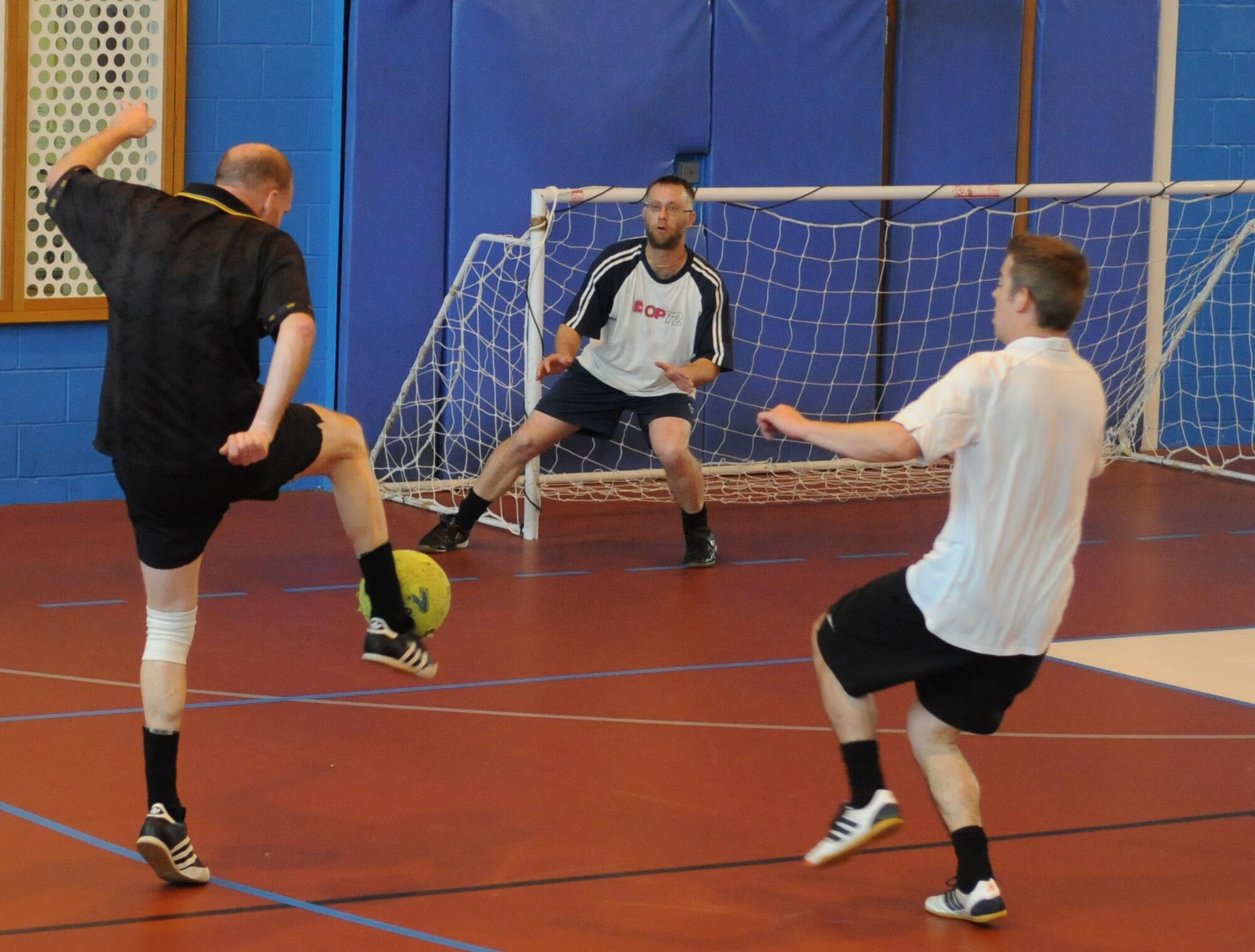Gary Butcher, left, 100th Force Support Squadron accounting technician from Cambridge, England, attempts a goal as Barry King, center, 100th Civil Engineer Squadron storekeeper from Lakenheath, England, moves to defend during an indoor soccer championship May 6, 2014, at RAF Mildenhall, England. The 100th CES team won 8-6 to take home the trophy. (U.S. Air Force photo by Tech. Sgt. Neal X. Joiner/Released)