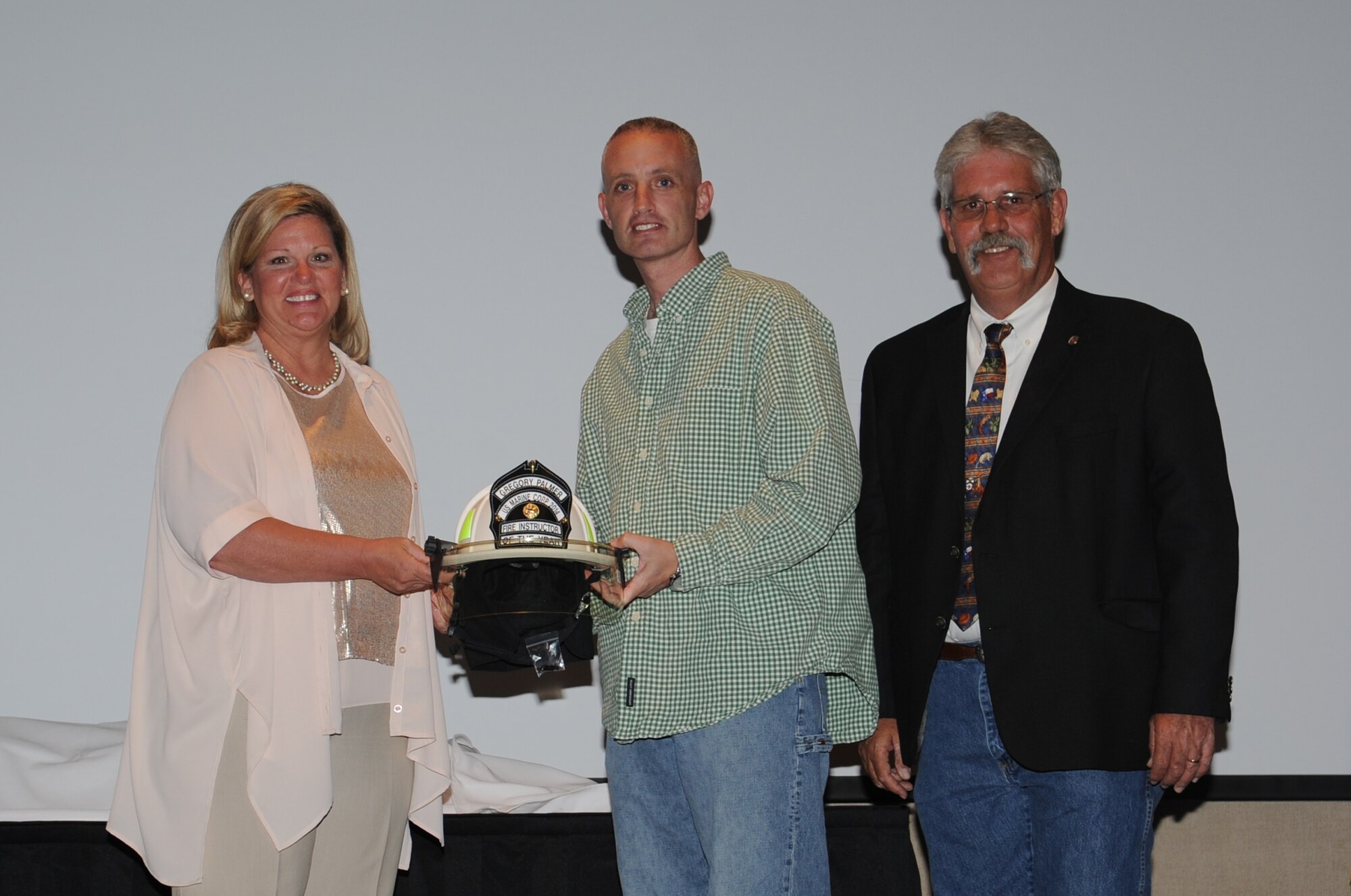 SAN ANGELO, Texas -- Lenna Boggs, Tom Smith Fire Equipment president and CEO, left, and Mike Robertson, 312th Training Squadron Fire Academy Training Development Chief, right, present Marine Corps Gunnery Sgt. Gregory J. Palmer, Marine Corps Detachment Goodfellow, with the Tom Smith Fire Equipment Department of Defense Fire Academy Fire Instructor of the Year during the Military Firefighter Heritage Foundation’s Annual Firefighter Muster at the McNease Convention Center here May 3. Boggs presented a member of each service with the award. (U.S. Air Force photo/ Staff Sgt. Laura R. McFarlane)