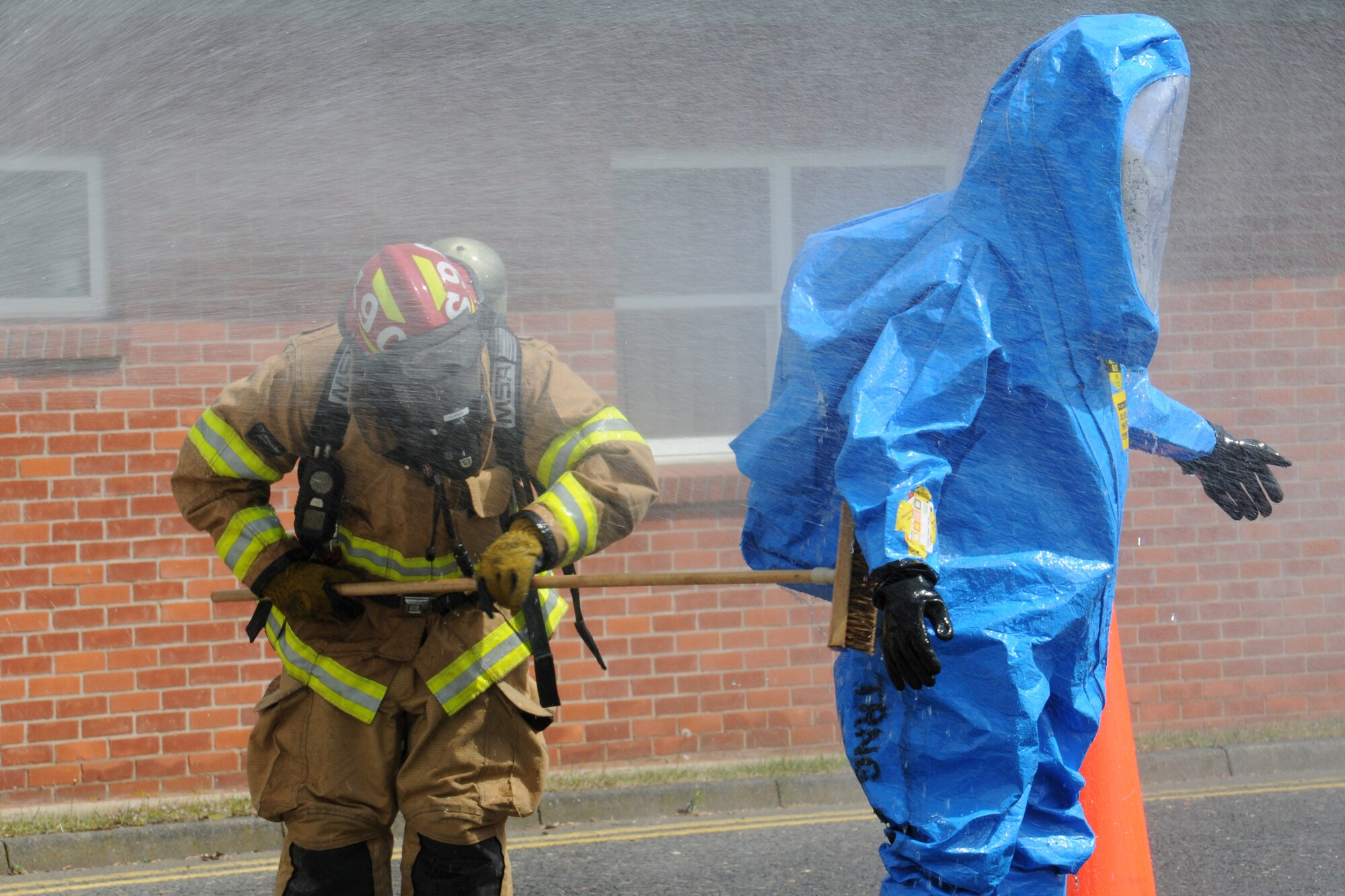 U.S. Air Force Tech. Sgt. Trey Sanders, left, 100th Civil Engineer Squadron Fire Department firefighter from Temple, Texas, uses a broom and water to clean potentially hazardous chemicals from an emergency manager’s personal protective equipment during a hazardous materials exercise May 6, 2014, on RAF Mildenhall, England. The base exercises regularly to ensure emergency responders remain proficient for any real-world incidents. (U.S. Air Force photo by Gina Randall/Released)