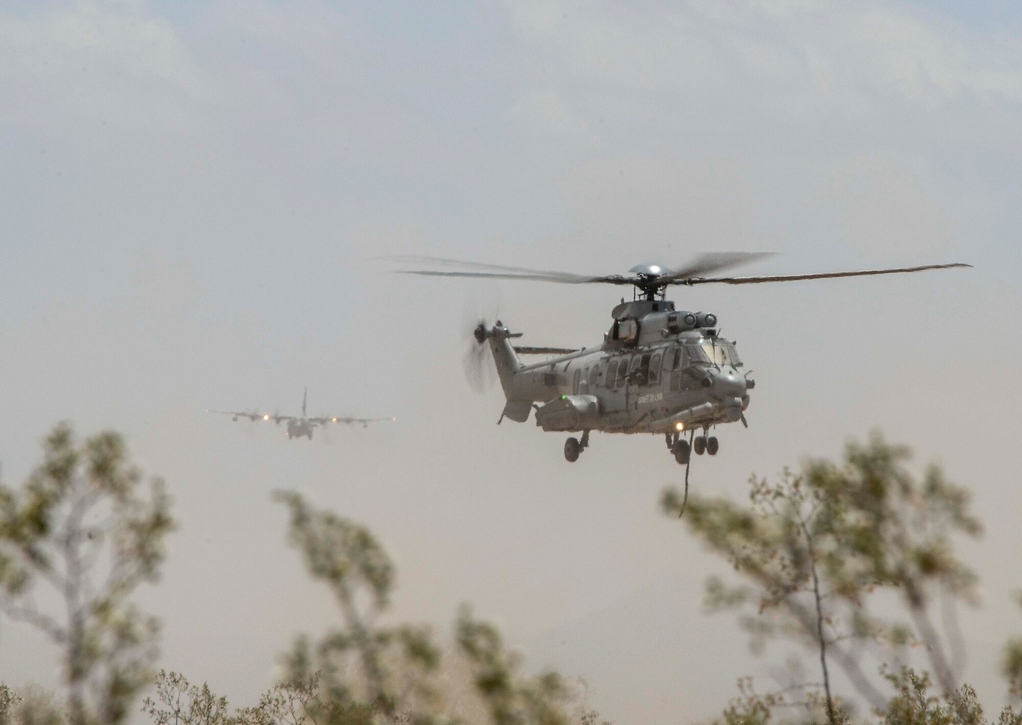 A French Eurocopter EC-735 Caracal hovers while personnel aboard prepare to fastrope down, and a HC-130J prepares to land during Exercise ANGEL THUNDER on May 07, 2014 at Davis-Monthan Air Force Base, Ariz. ANGEL THUNDER 2014 is the largest and most realistic joint service, multinational, interagency combat search and rescue exercise designed to provide training for personnel recovery assets using a variety of scenarios to simulate deployment conditions and contingencies. Personnel recovery forces will train through the full spectrum of personnel recovery capabilities with ground recovery personnel, air assets, Special Forces teams and federal agents. (U.S. Air Force photo by Staff Sgt. Adam Grant/Released)