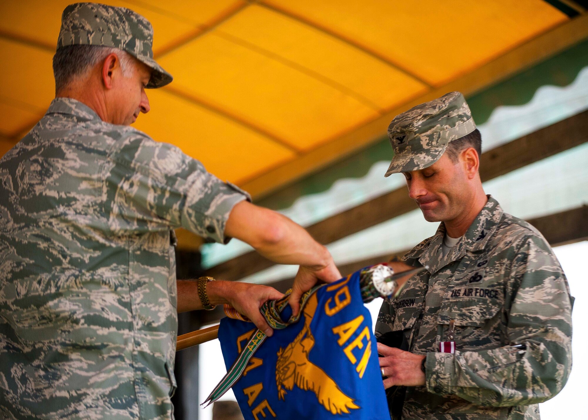 U.S. Air Force Brig. Gen. Roger H. Watkins, 379th Air Expeditionary Wing commander, and Col. Gregory Anderson, 64th Air Expeditionary Group commander, roll the 64th AEG guidon during an deactivation ceremony at an undisclosed location in Southwest Asia, May 1, 2014. The 64th AEG was activated in September 2005, and was deactivated in part of a downsizing in the region. (U.S. Air Force photo by Master Sgt. Jason Kauffung)