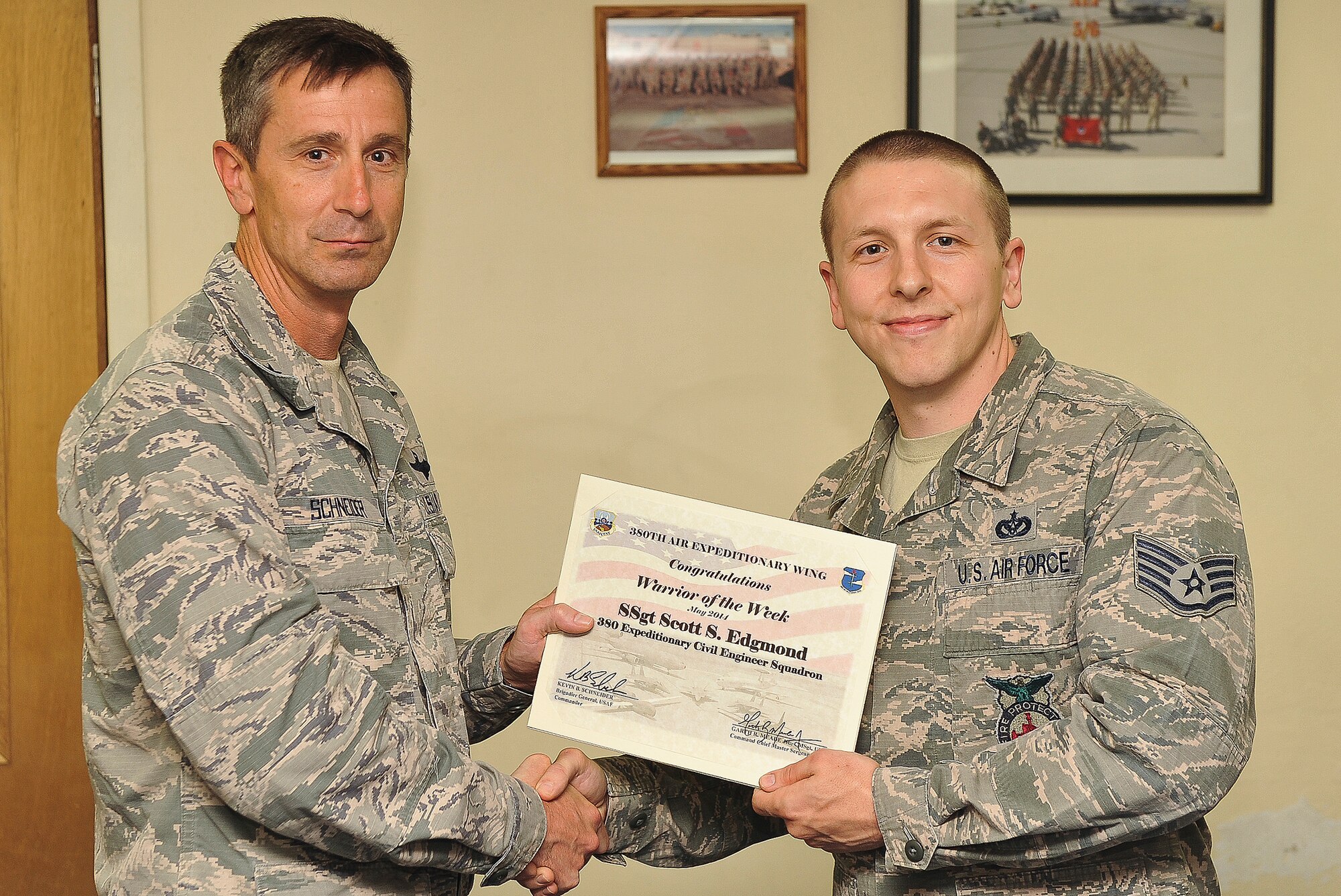 Air Force Brig. Gen. Kevin Schneider, 380th Air Expeditionary Wing commander, presents Staff Sgt. Scott Edgmond, 380th Air Expeditionary Civil Engineer Squadron fire protection assistant chief of training, with a warrior of the week certificate at an undisclosed location in Southwest Asia, May 6, 2014. Edgmond is a native of Spokane, Wash., and is deployed from Misawa Air Base, Japan.(U.S. Air Force photo byTech. Sgt. Russ Scalf/Released)