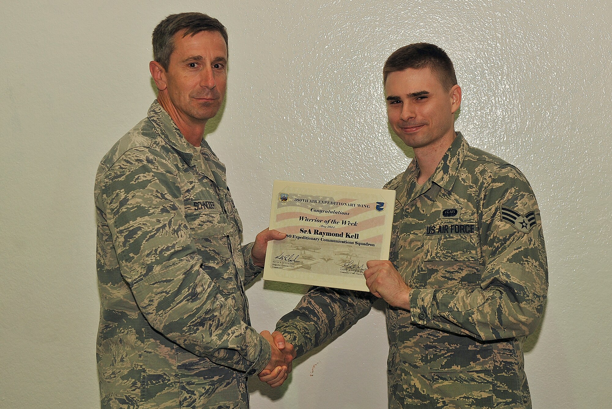 Air Force Brig. Gen. Kevin Schneider, 380th Air Expeditionary Wing commander, presents Senior Airman Raymond Kell, 380th Air Expeditionary Communications Squadron cyber transport systems specialist, with a warrior of the week certificate at an undisclosed location in Southwest Asia, May 6, 2014. Kell is a native of San Diego, Calif., and is deployed from Eielson, Air Force Base, Alaska.  (U.S. Air Force photo byTech. Sgt. Russ Scalf/Released)