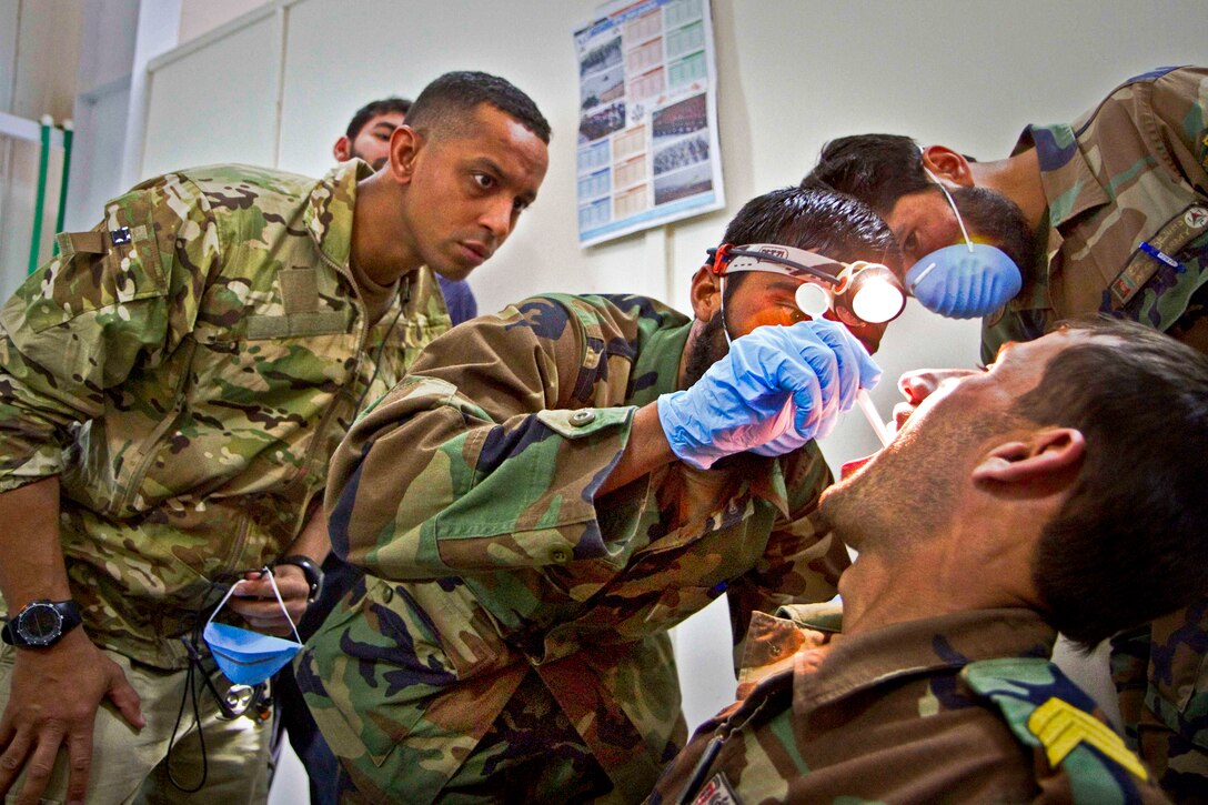 U.S. Army Capt. Abby Raymond, left, looks over the shoulder of an Afghan medic as he performs an oral exam on a commando during a basic dental class on Forward Operating Base Thunder in Paktya province, Afghanistan, July 21, 2013. Raymond, a dentist, is assigned to the 101st Airborne Division's 4th Brigade Combat Team.  
