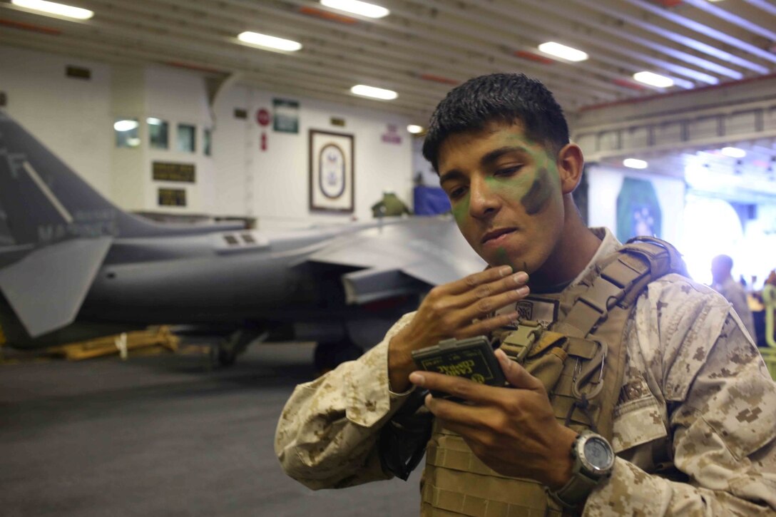 Lance Cpl. Christian Salazarvargas, a rifleman with Golf Company, Battalion Landing Team 2nd Battalion, 1st Marines (BLT 2/1), 11th Marine Expeditionary Unit applies camouflage paint to his face in the hangar bay of the USS Makin Island before  conducting an airfield seizure during Composite Training Unit Exercise (COMPTUEX), off the coast of San Diego, May 10, 2014.  The 11th MEU and Amphibious Squadron 5 team conduct COMPTUEX to hone mission essential tasks, execute specified MEU and Amphibious Ready Group operations, and establish the foundation for a cohesive warfighting team for future exercises and operations. (U.S. Marine Corps photo by Lance Cpl. Evan R. White/RELEASED)