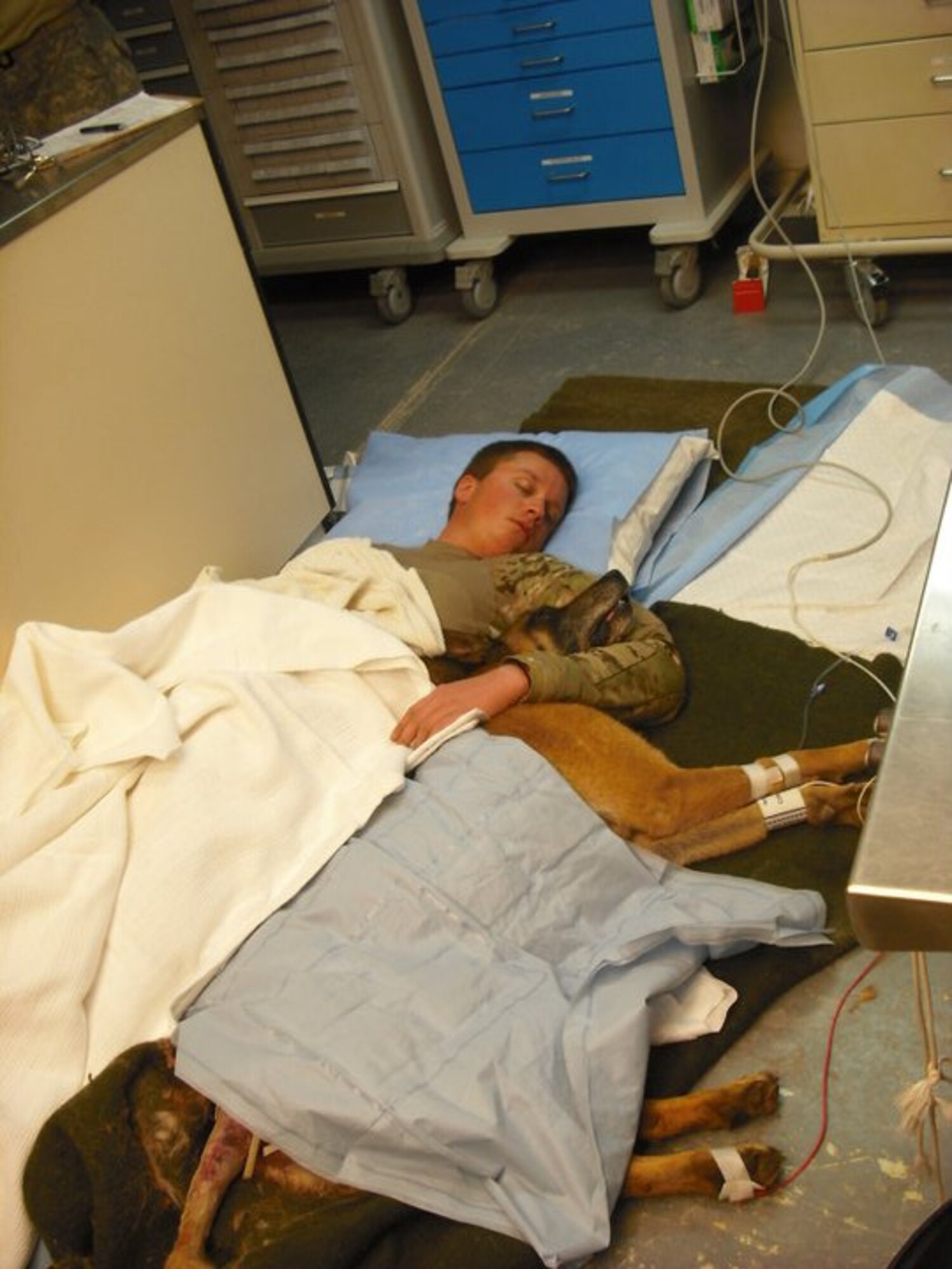 Navy Petty Officer 2nd Class Ryan Lee, master at arms, and Petty Officer 1st Class Valdo, working dog, sleep on a hospital floor in Kandahar, Afghanistan. Valdo and Lee both were wounded by shrapnel in a rocket propelled grenade attach in Bala Murghab District, Badghis Province, Afghanistan, April 4, 2011. (U.S. Air Force photo by Master Sgt. Kevin Wallace/RELEASED)
