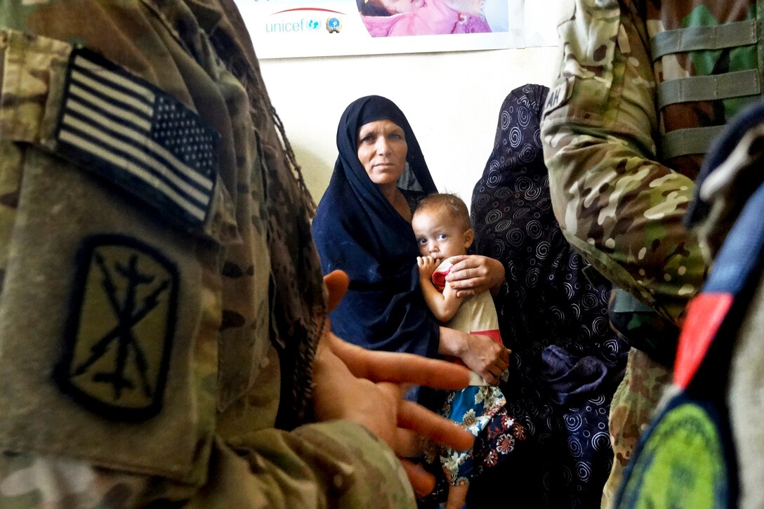An Afghan mother and child watch as U.S. troops meet with the director of a nutritional center within the Farah Feeding Center in Farah City, Afghanistan, July 13, 2013. The troops are assigned to Provincial Reconstruction Team Farah, 2nd Battalion, 12th Field Artillery Security Force.  
