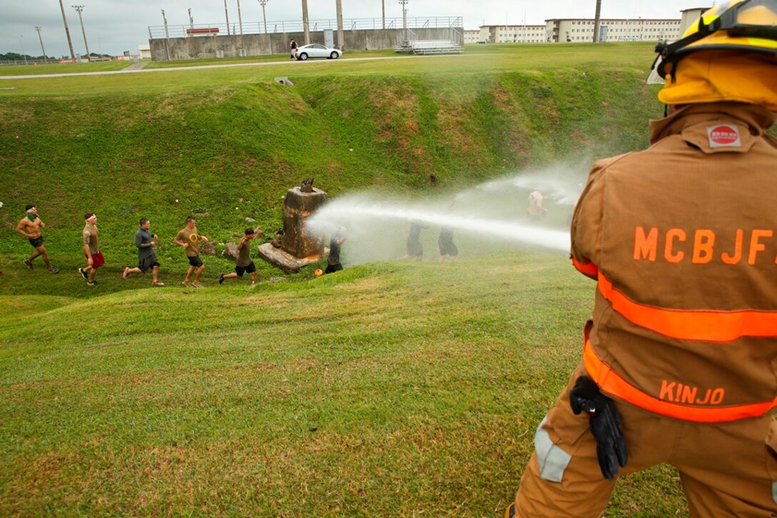 A firefighter with the Marine Corps Installations Pacific Fire and Emergency Services sprays water on participants May 10 during the Single Marine Program’s second annual Bushido Mud Run at Camp Hansen. More than 2,000 people gathered at Camp Hansen’s parade field to take part in the race. 