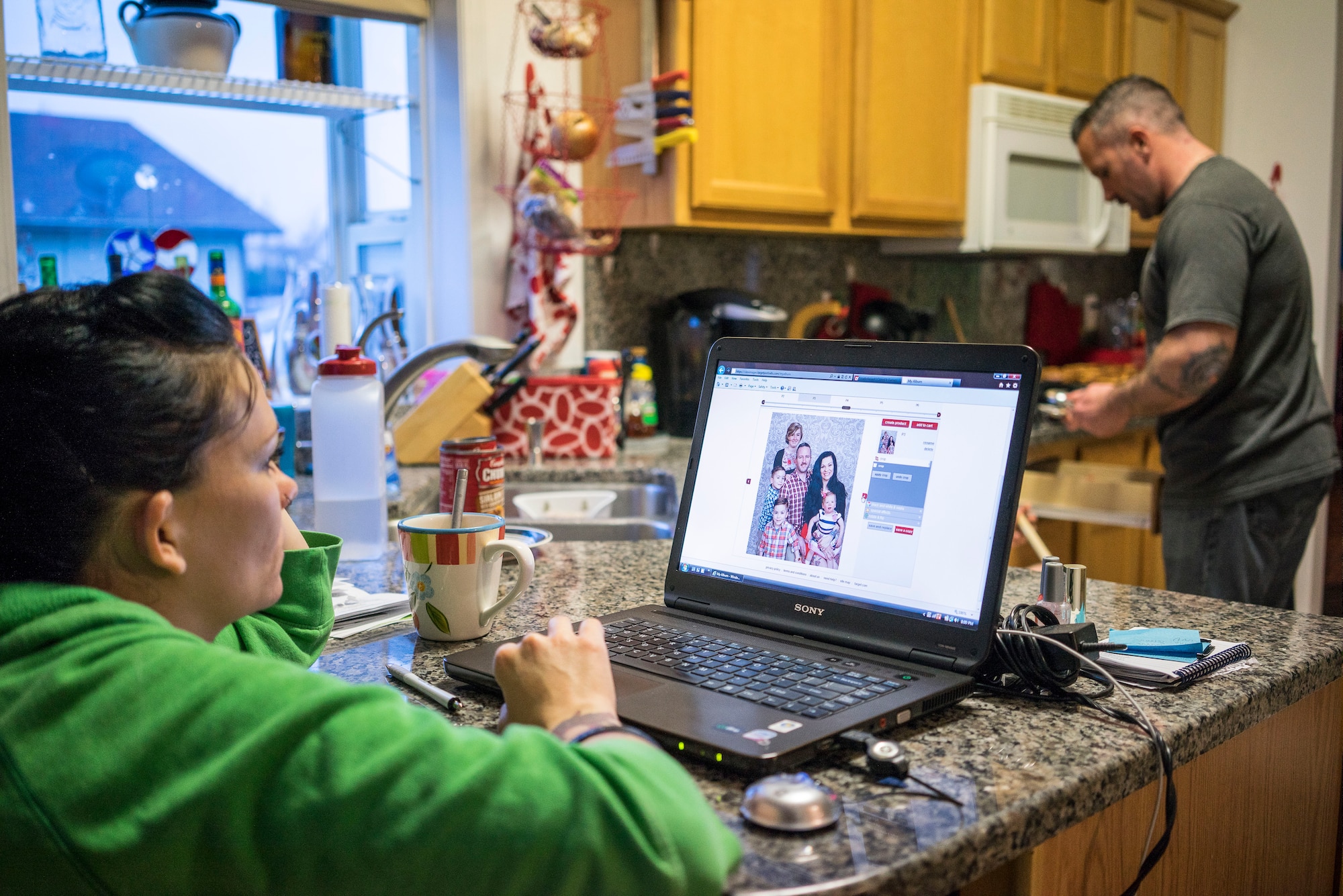 Tech. Sgt. Jamie Meadows-Valley browses new family photos while her husband Master Sgt. Ernie Valley prepares supper at their home in Mountain Home, Idaho. The family had new photos taken while Ernie's daughter Jewel was visiting, so they had everyone in the photo, including their twin boys and newly adopted daughter, Oleksandra. (U.S. Air Force photo/Tech. Sgt. Samuel Morse)