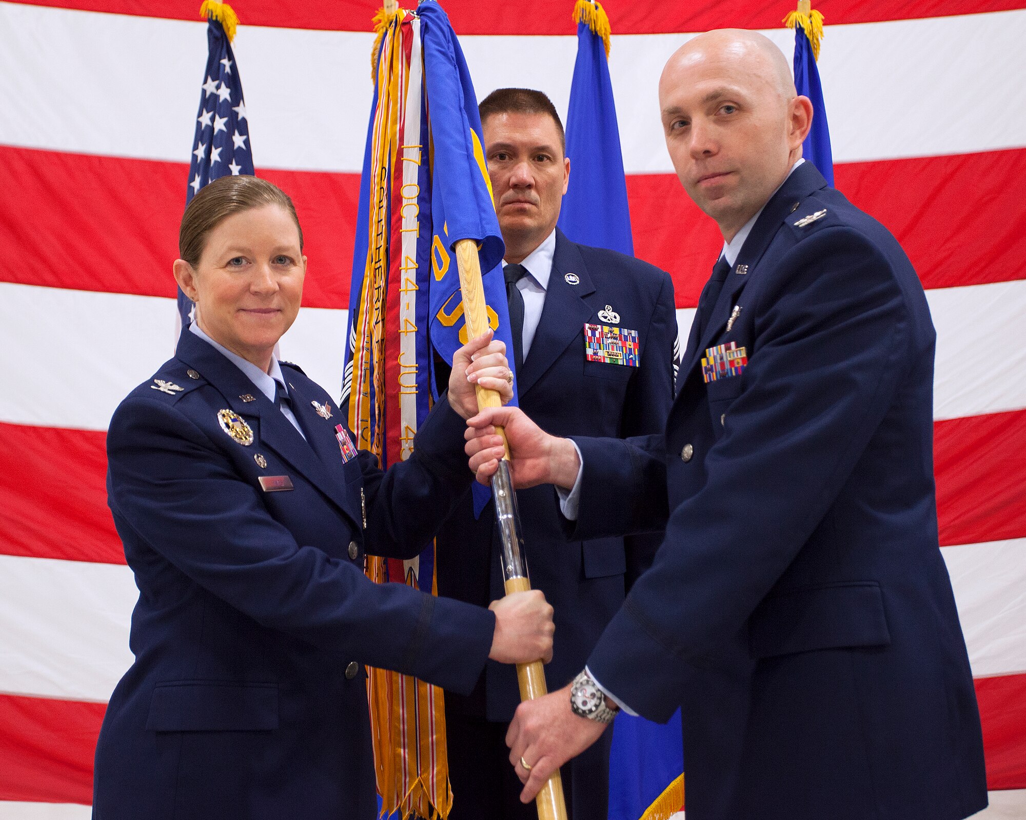 Col. Tracey Hayes, 90th Missile Wing commander, passes the 90th Operations Group guidon to Col. Ron Allen as he assumes command of the group during a change-of-command ceremony in the 37th Helicopter Squadron hanger, Bldg. 1250, at F.E. Warren Air Force Base, Wyo., May 9, 2014. Chief Master Sgt. James Dye, 90th OG superintendent, stands by to take the guidon back from Allen. (U.S. Air Force photo by R.J. Oriez)
