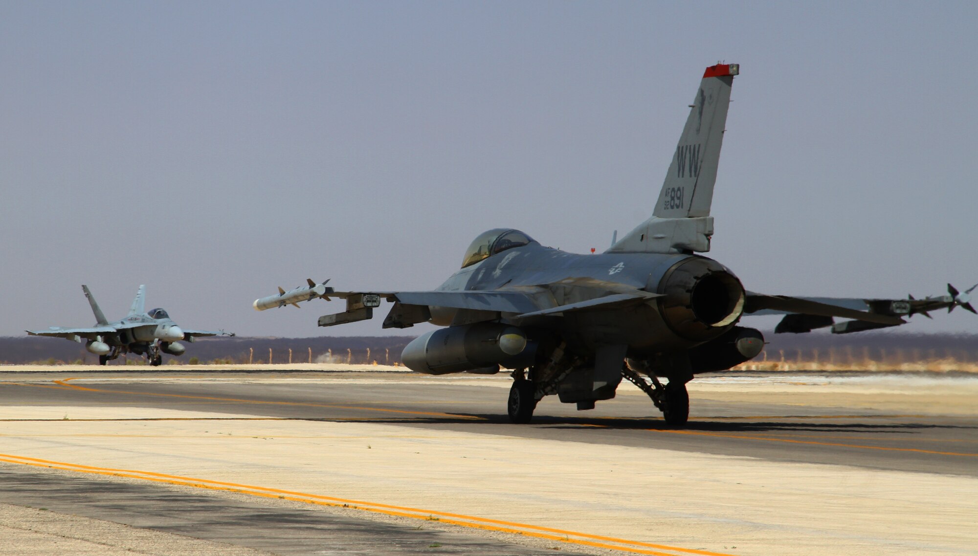 An F-16 Fighting Falcon from the 13th Fighter Squadron at Misawa Air Base, Japan, and an F-18 Hornet from the U.S. Marine Corps, Marine Air Group 50, await takeoff clearance during Exercise Eager Tiger May 12, 2014, at an air base in northern Jordan. The pilots and aircrews had just participated in a scramble competition to see which service could prepare for takeoff the fastest. (U.S. Air Force photo by Staff Sgt. Tyler McLain/Released)