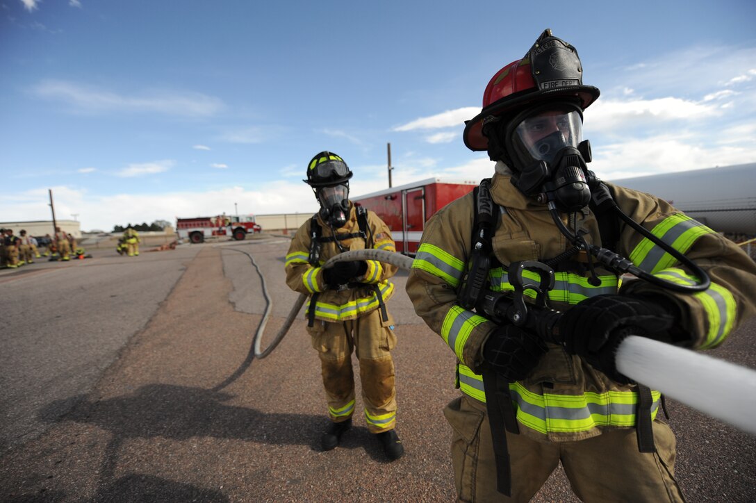 PETERSON AIR FORCE BASE, Colo. – Staff Sgt. Robert Jones, right, 21st Civil Engineer Squadron fire protection technician, and Chief Master Sgt. Richard Redman, 21st Space Wing command chief, spray a hose at a target during training exercise May 9 here. The exercise consisted of the unofficial firefighter physical fitness test and a confidence burn. (U.S. Air Force photo/Staff Sgt. Jacob Morgan)