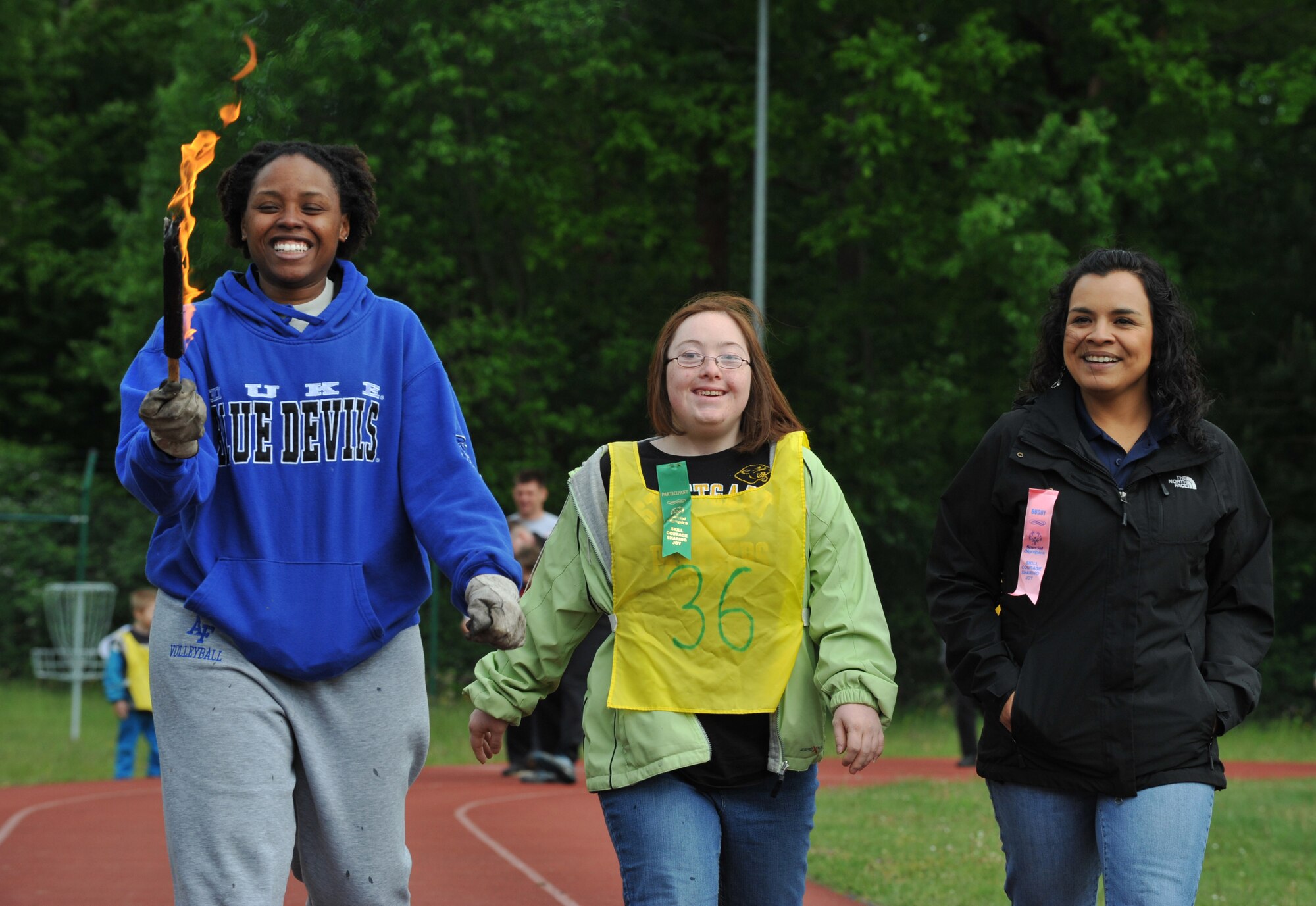 Jessica Lawrence (middle), daughter of Army Lt. Col. Ryan Lawrence, walks with her buddy, Felicia Escalante (right), and the torch bearer during the opening ceremony of the 2014 Spring Special Olympics began in Pulaski Park, May 9, 2014. This year’s Special Olympics consisted of events such as track and field, soccer, volleyball, basketball, softball, arts and crafts and karaoke; there were also non-competitive events for children ages five to seven who weren’t able compete yet according to the rules. (U.S. Air Force photo/Senior Airman Hailey Haux)