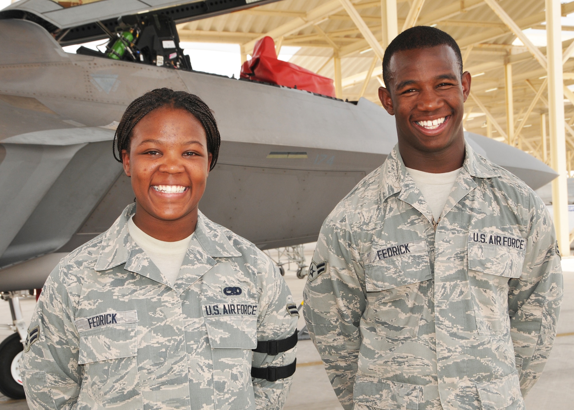 Air Force Airmen First Class Celecca and Tevin Fedrick stand near an F-22 Raptor fighter aircraft during a break in their work schedule. The deployed sister and brother are serving with the 380th Air Expeditionary Wing at an undisclosed location in Southwest Asia. (U.S. Air Force photo by Senior Master Sgt. Eric Peterson/Released)
